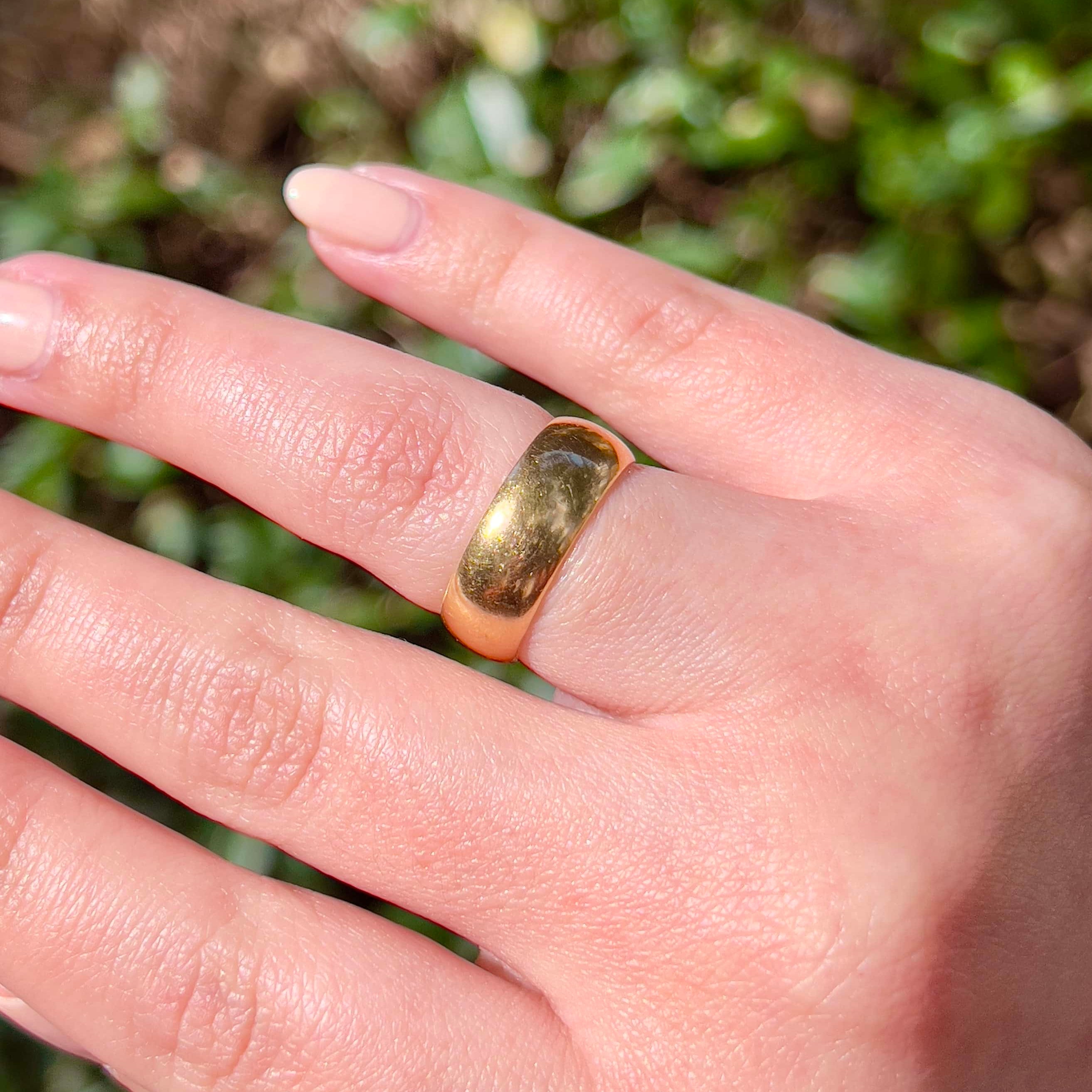 A Victorian gold band with a patina on a hand with a green background.