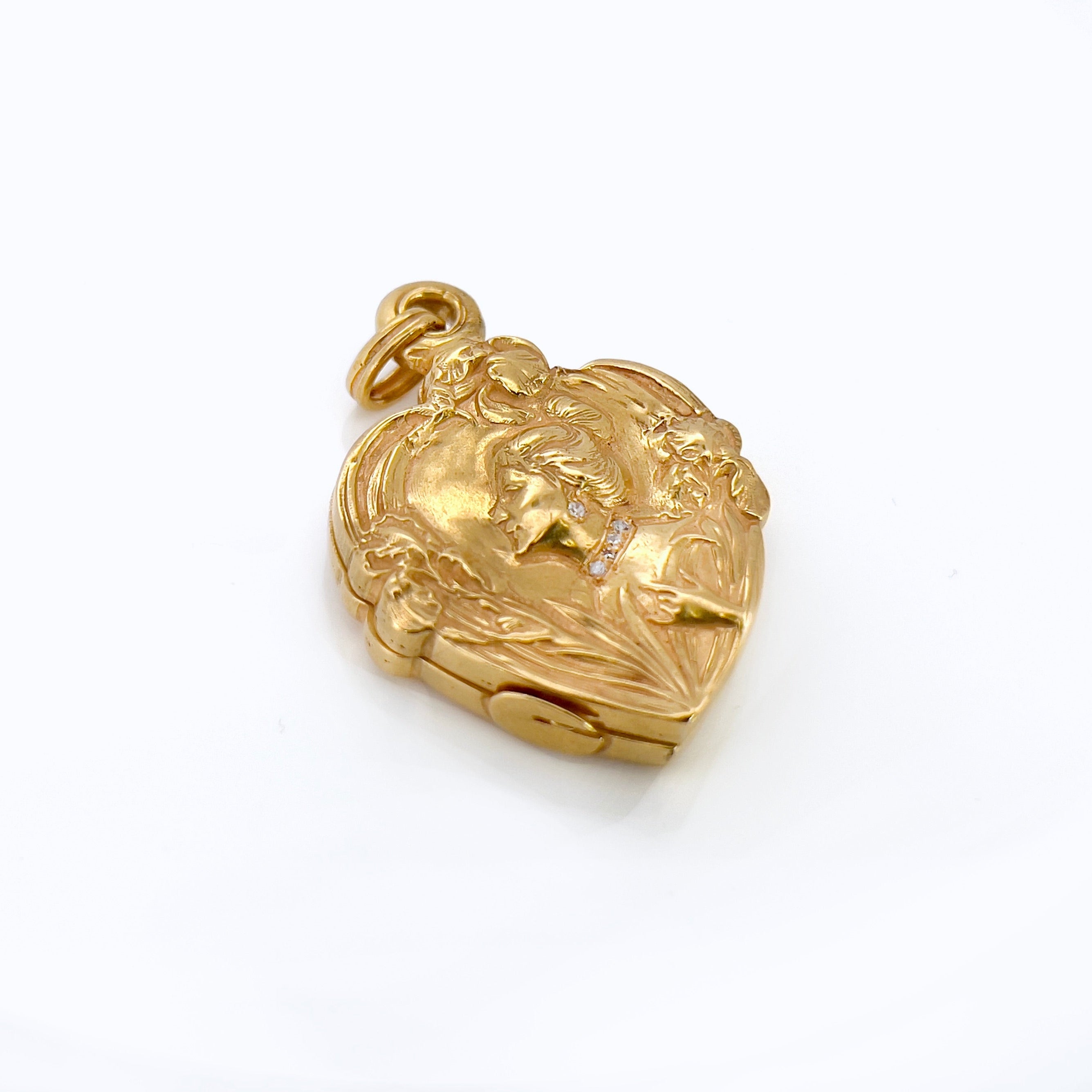 An Art Nouveau heart-shaped locket with gold detailing, featuring a central figure with a bun and flowers on the front, on a white background.