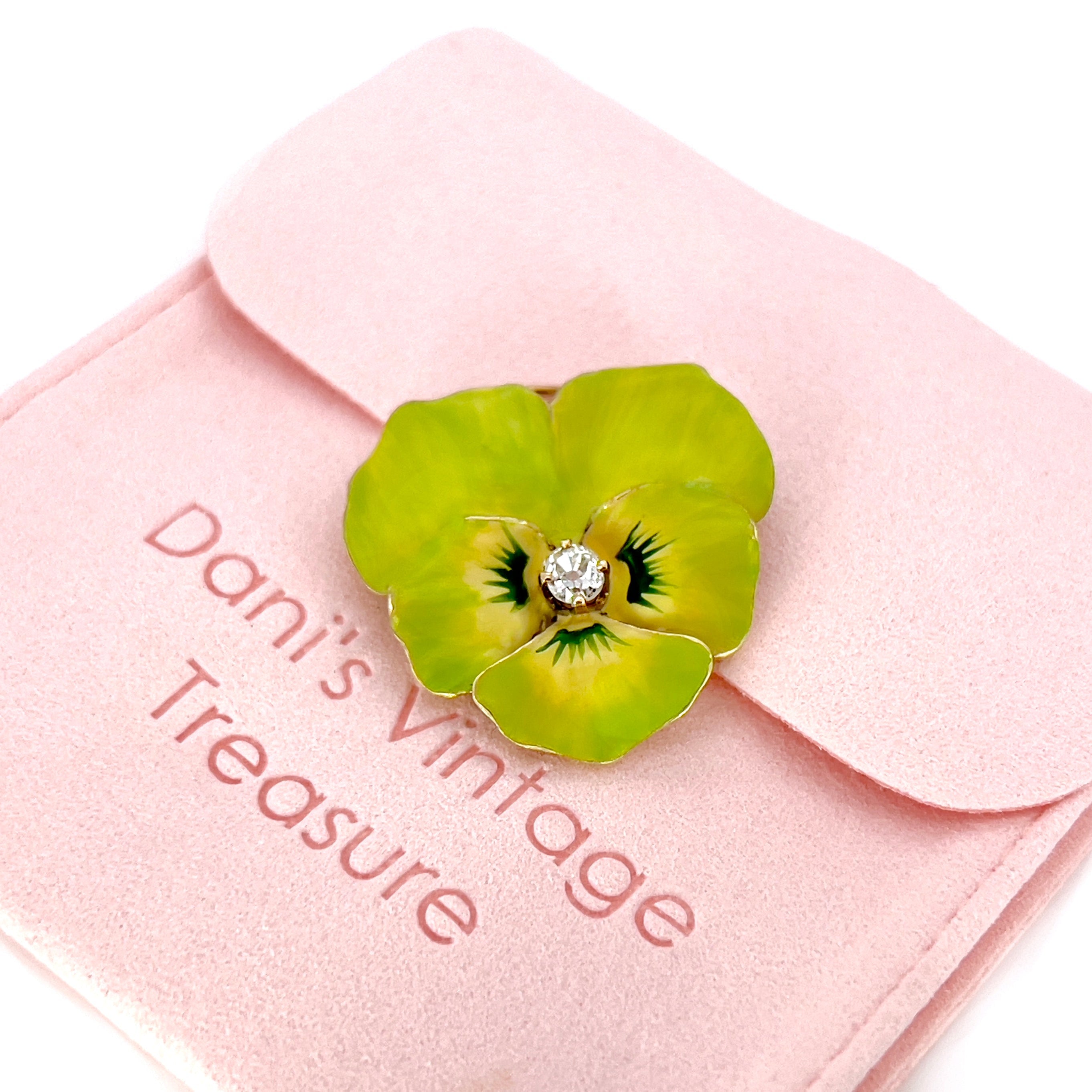 A Victorian lime green Pansy brooch with a 14K yellow gold setting and a central old mine cut diamond, on a pink pouch.