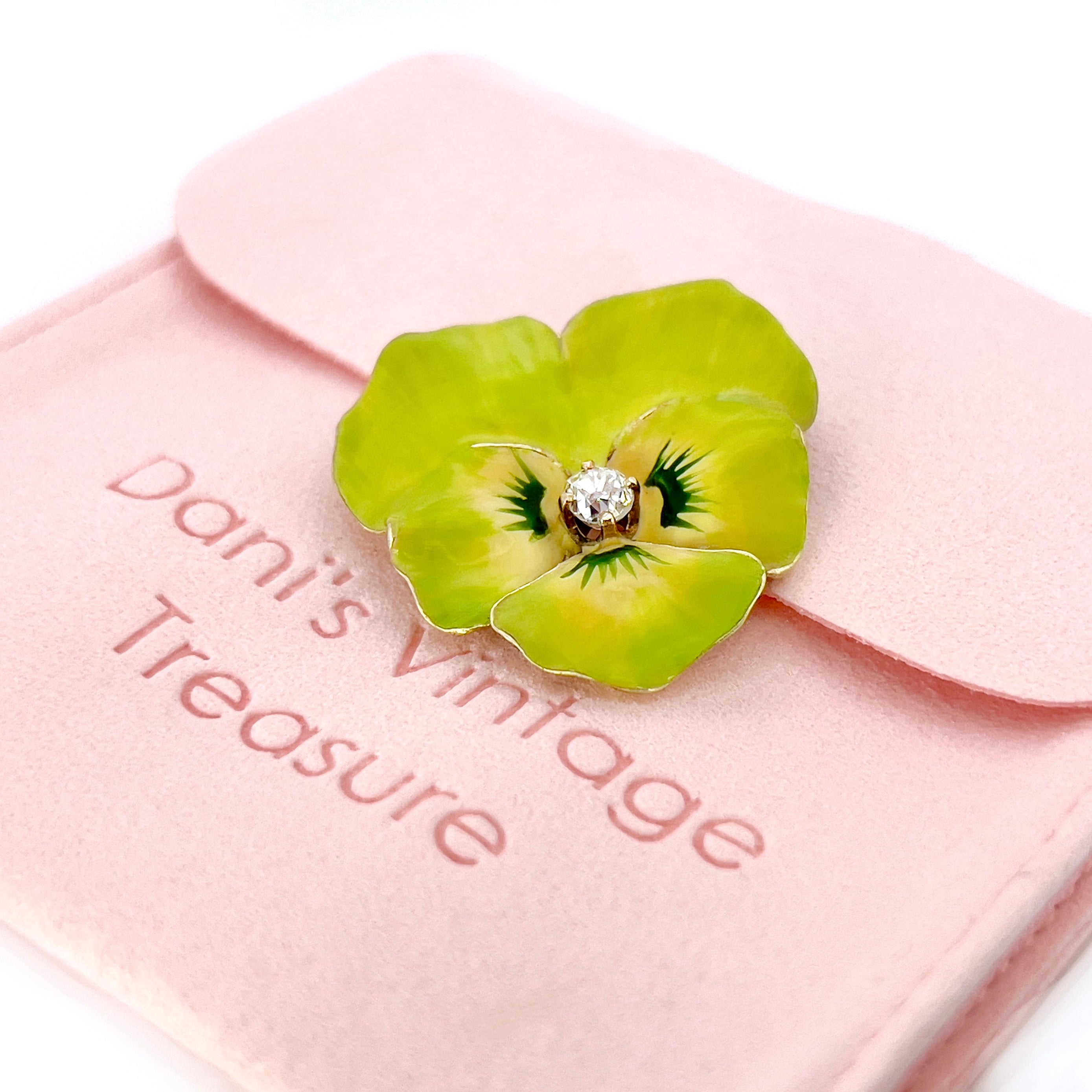 A Victorian lime green Pansy brooch with a 14K yellow gold setting and a central old mine cut diamond, on a pink pouch.