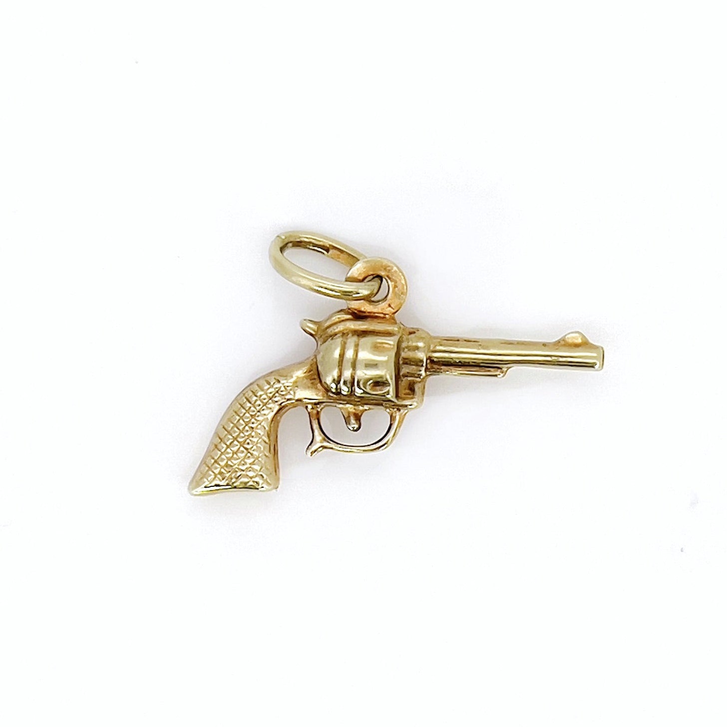 A vintage gold revolver charm with a aged patina, featuring a small ring as a bail.