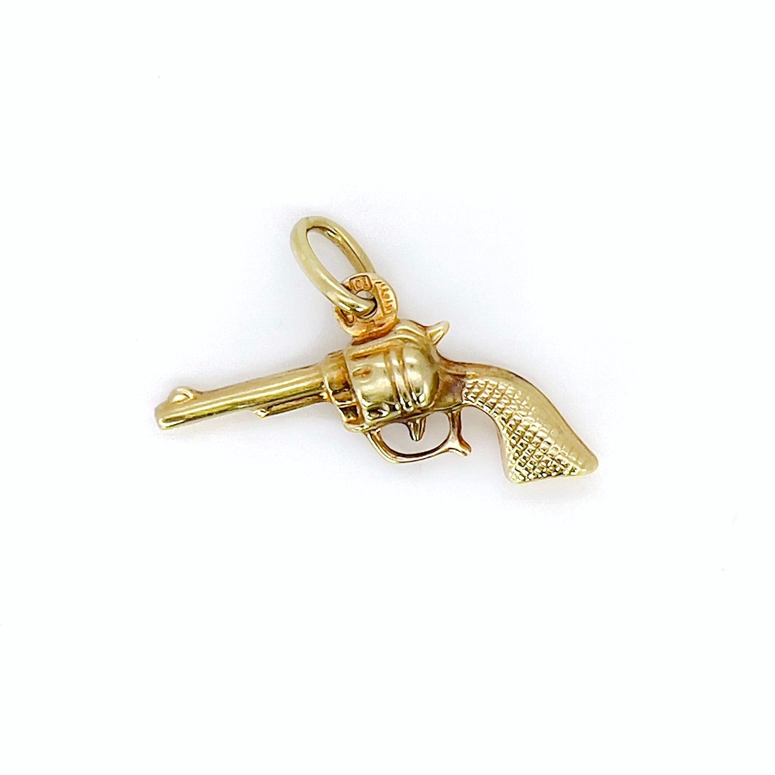 A vintage gold revolver charm with a aged patina, featuring a small ring as a bail.