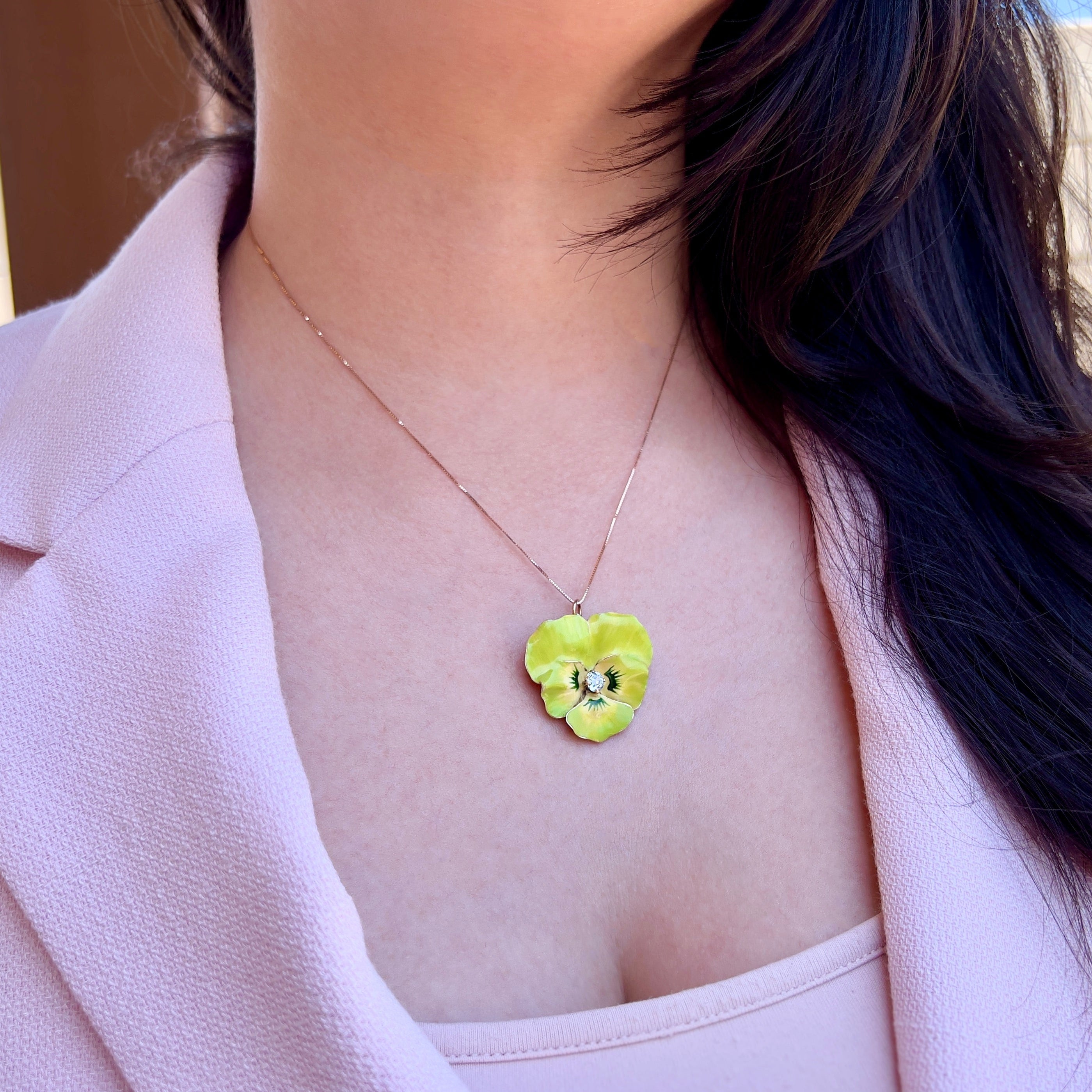 A person wearing a gold chain with a lime green pansy pendant.