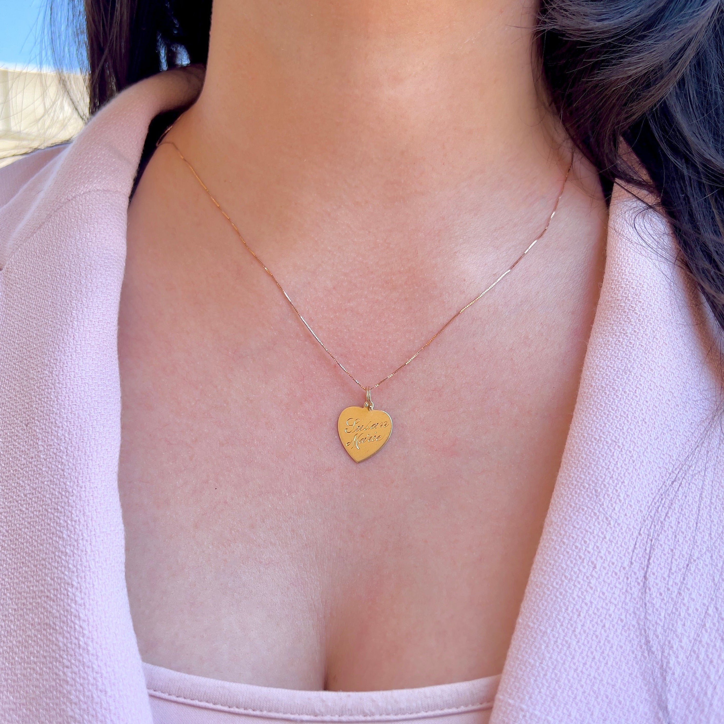 Close up of a person wearing a gold chain with a heart-shaped charm.