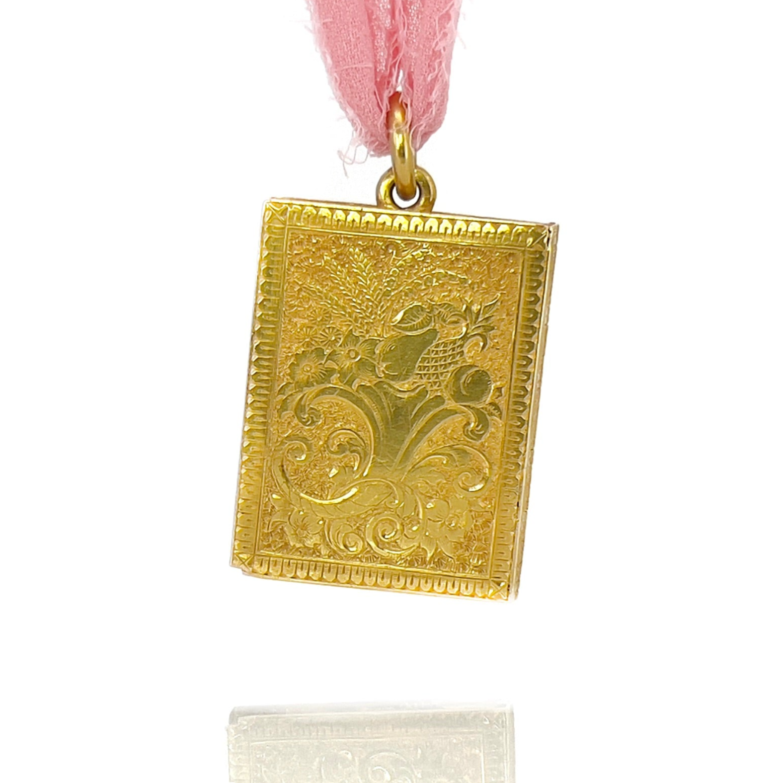 Gold victorian book locket with intricate design on a pink ribbon against a white background