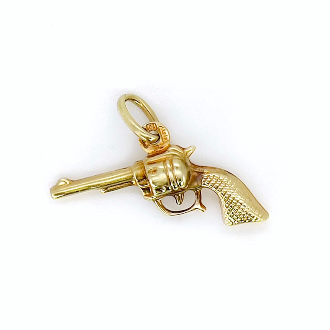A vintage gold revolver charm with a aged patina, featuring a small ring as a bail.