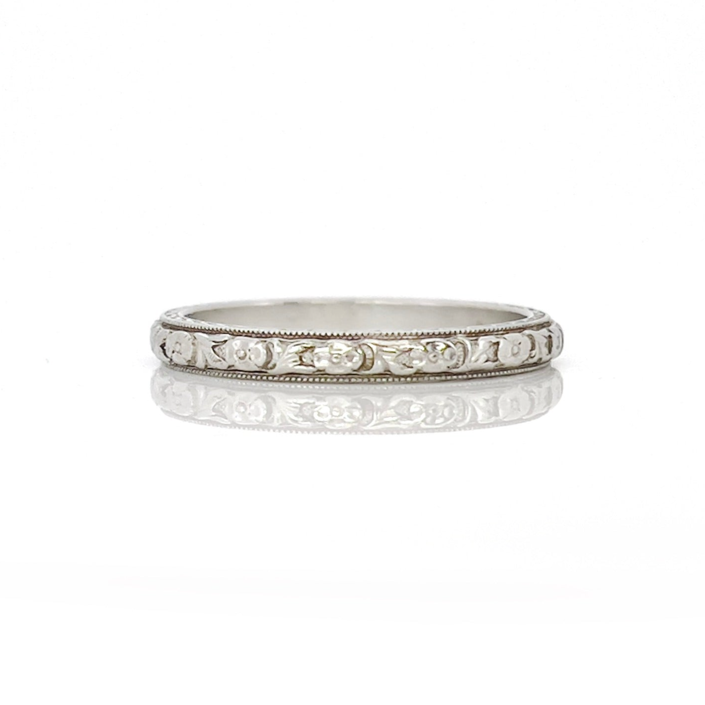 An white gold and platinum vintage wedding band with a floral design, engraved details on the sides, displayed against a white background.