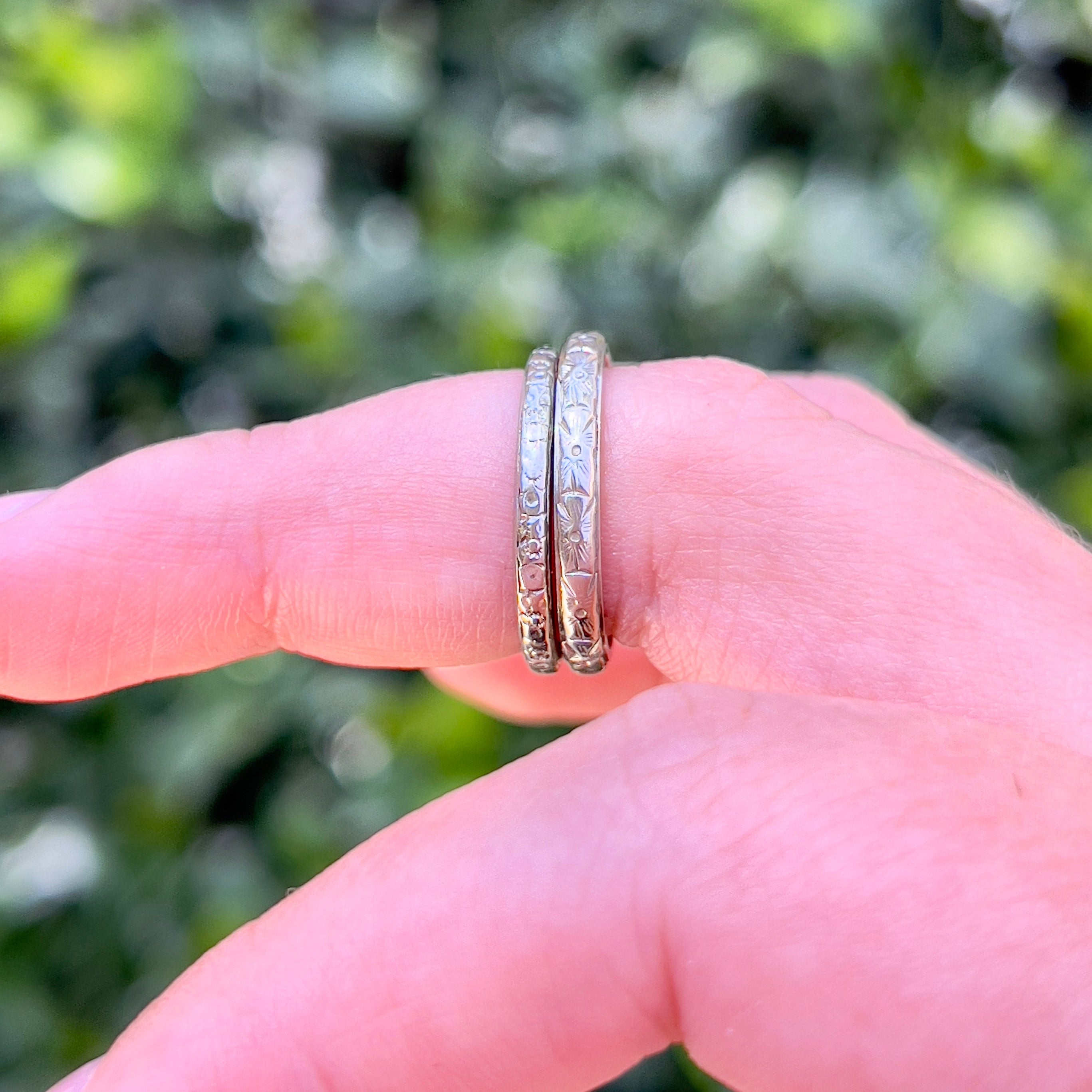 Two vintage white gold wedding bands modeled on a middle finger against an outdoor background.