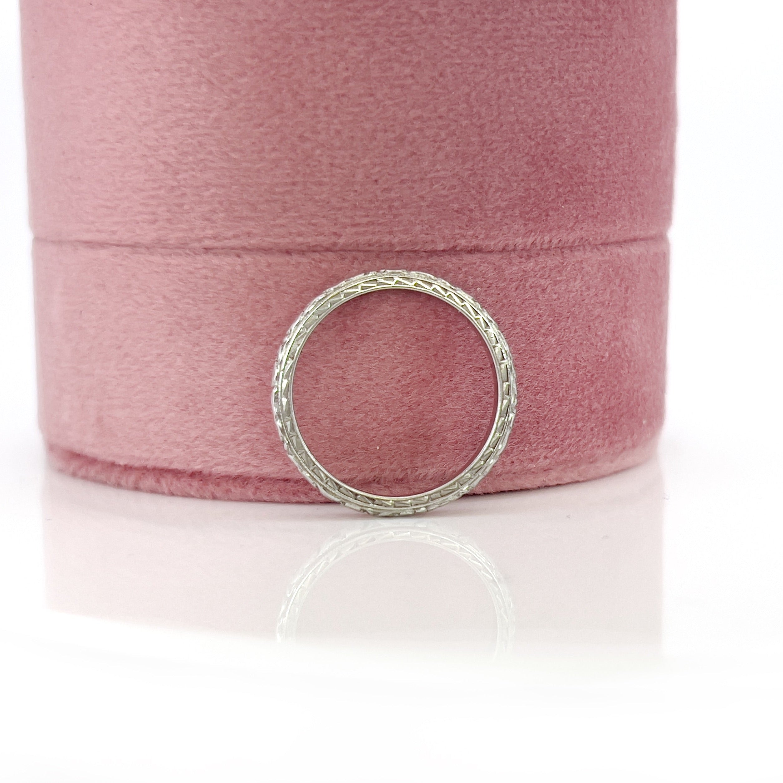 An white gold and platinum vintage wedding band with a floral design, engraved details on the sides, displayed against a white background.