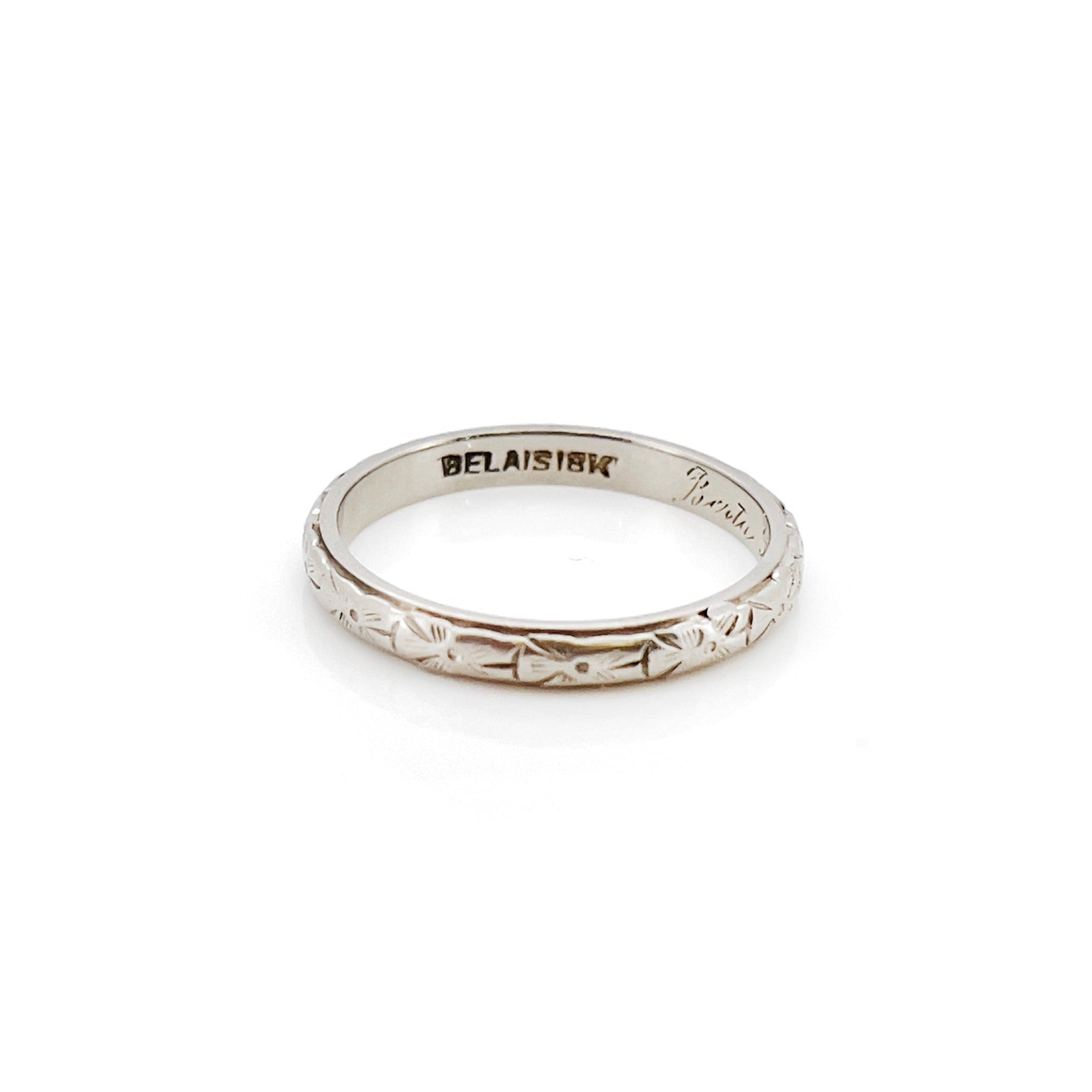 A vintage white gold wedding band with an intricate floral design and the name 'Berta' engraved inside.