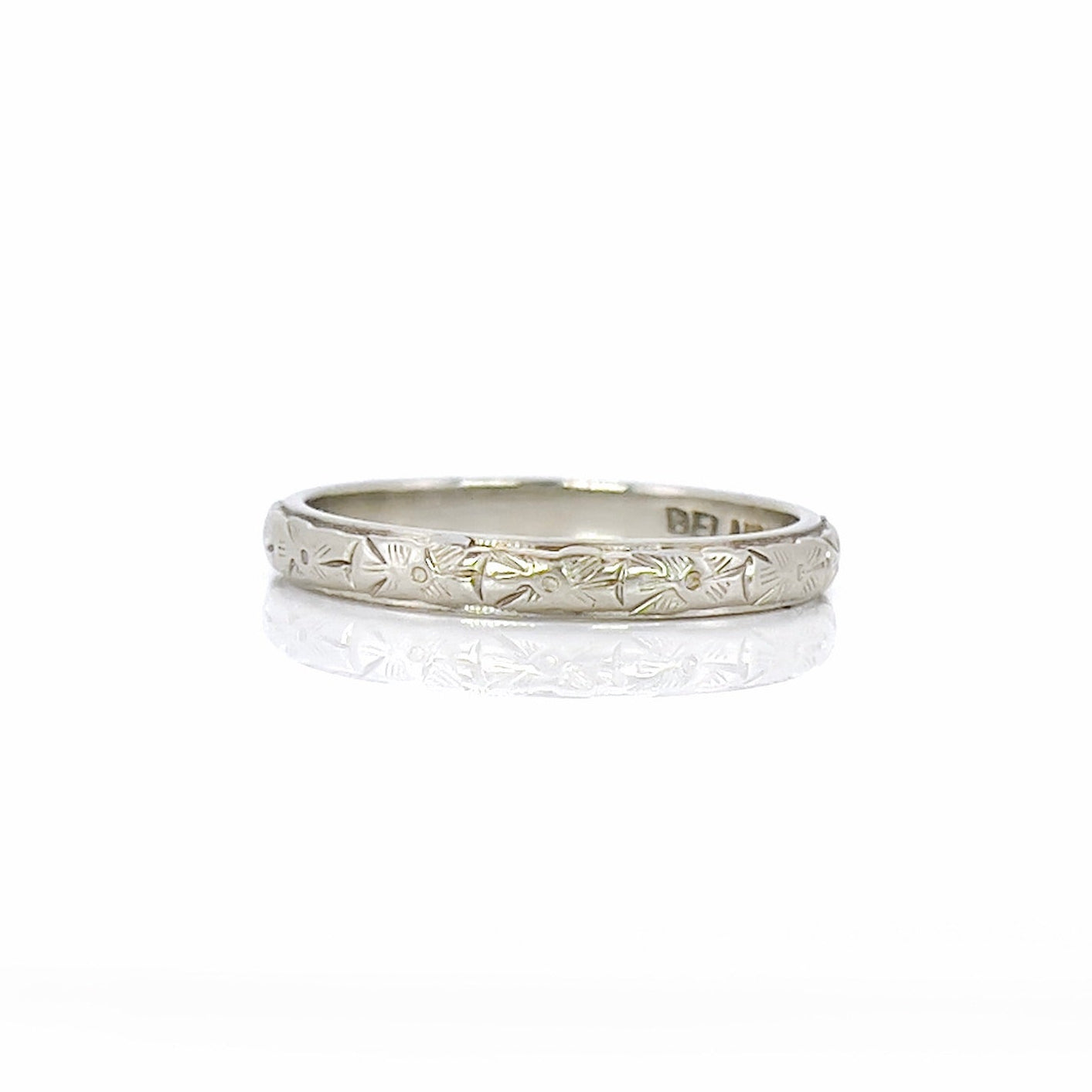 A vintage white gold wedding band with an intricate floral design and the name 'Berta' engraved inside.