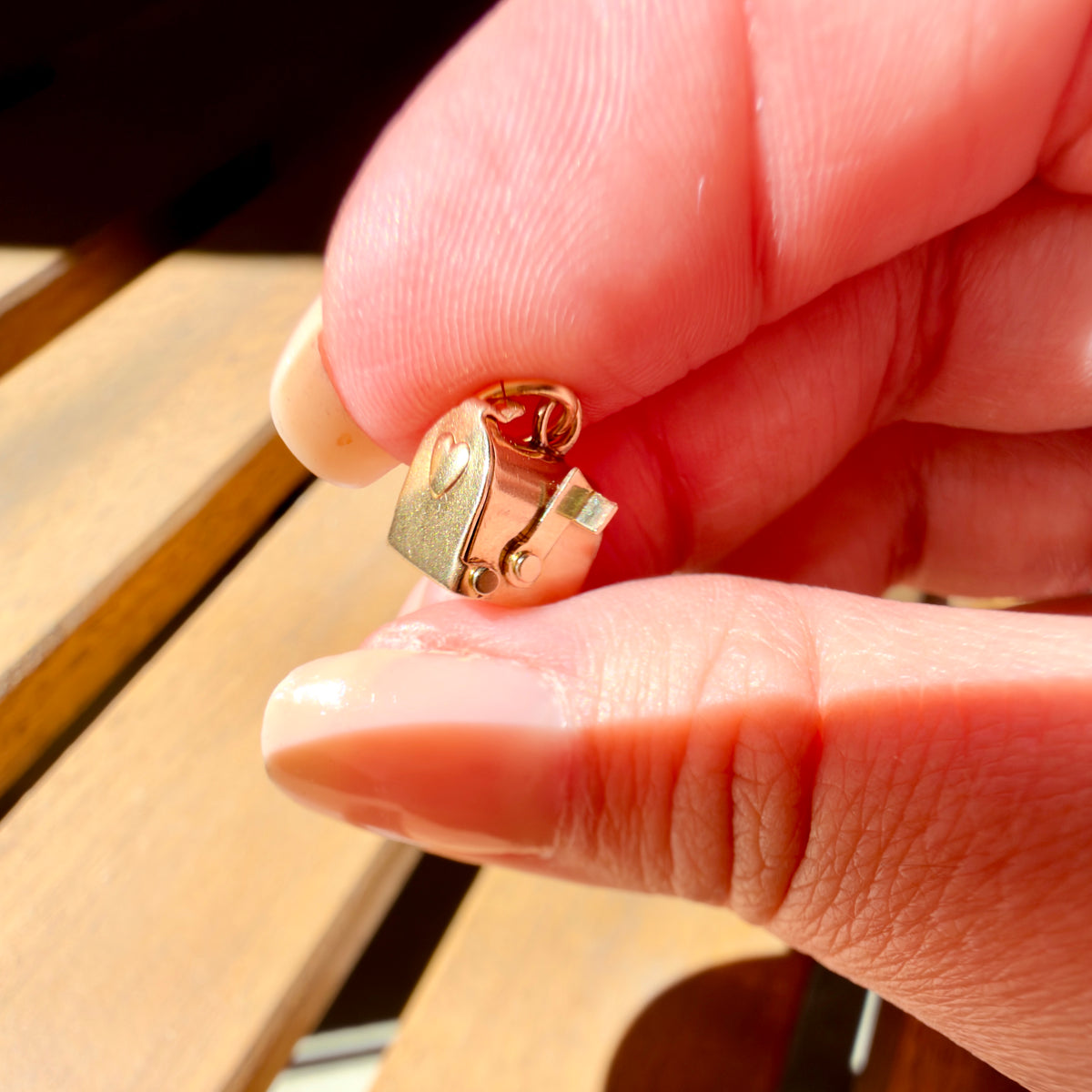 A close-up of a hand holding a small gold mailbox charm against a blurred wooden background.