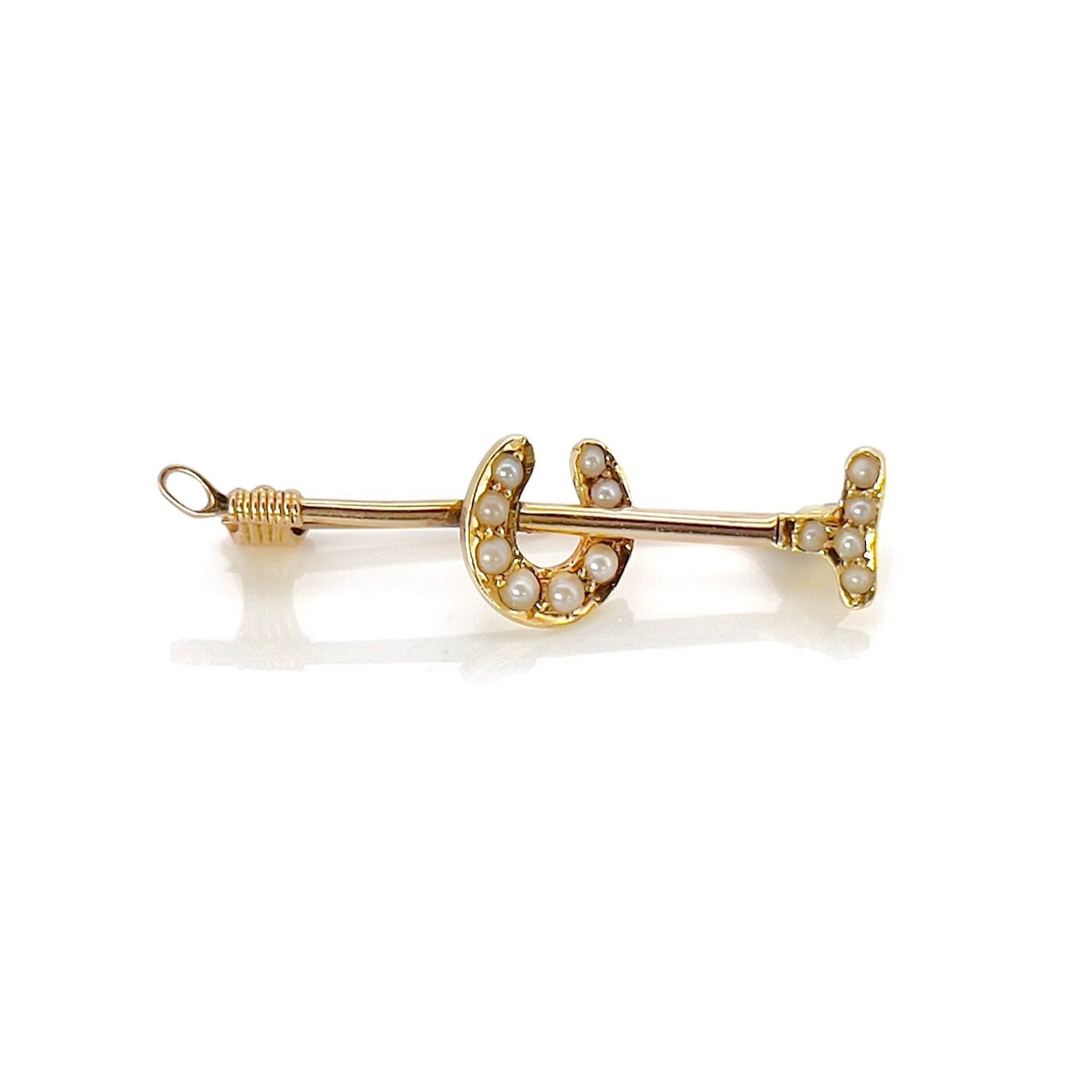 A victorian gold polo mallet and horseshoe brooch depicting small seed pearls, against a white background.