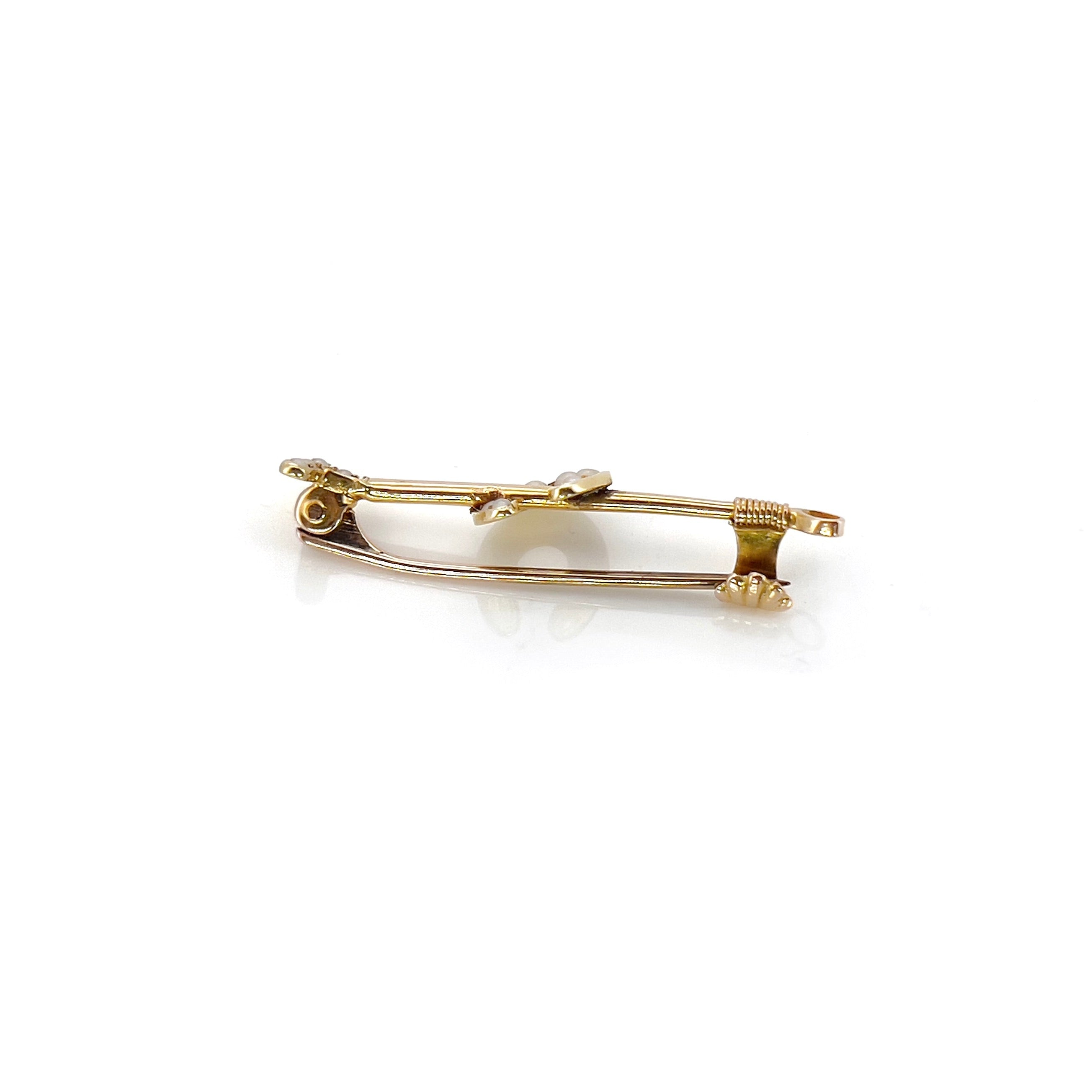 A victorian gold polo mallet and horseshoe brooch depicting small seed pearls, against a white background.