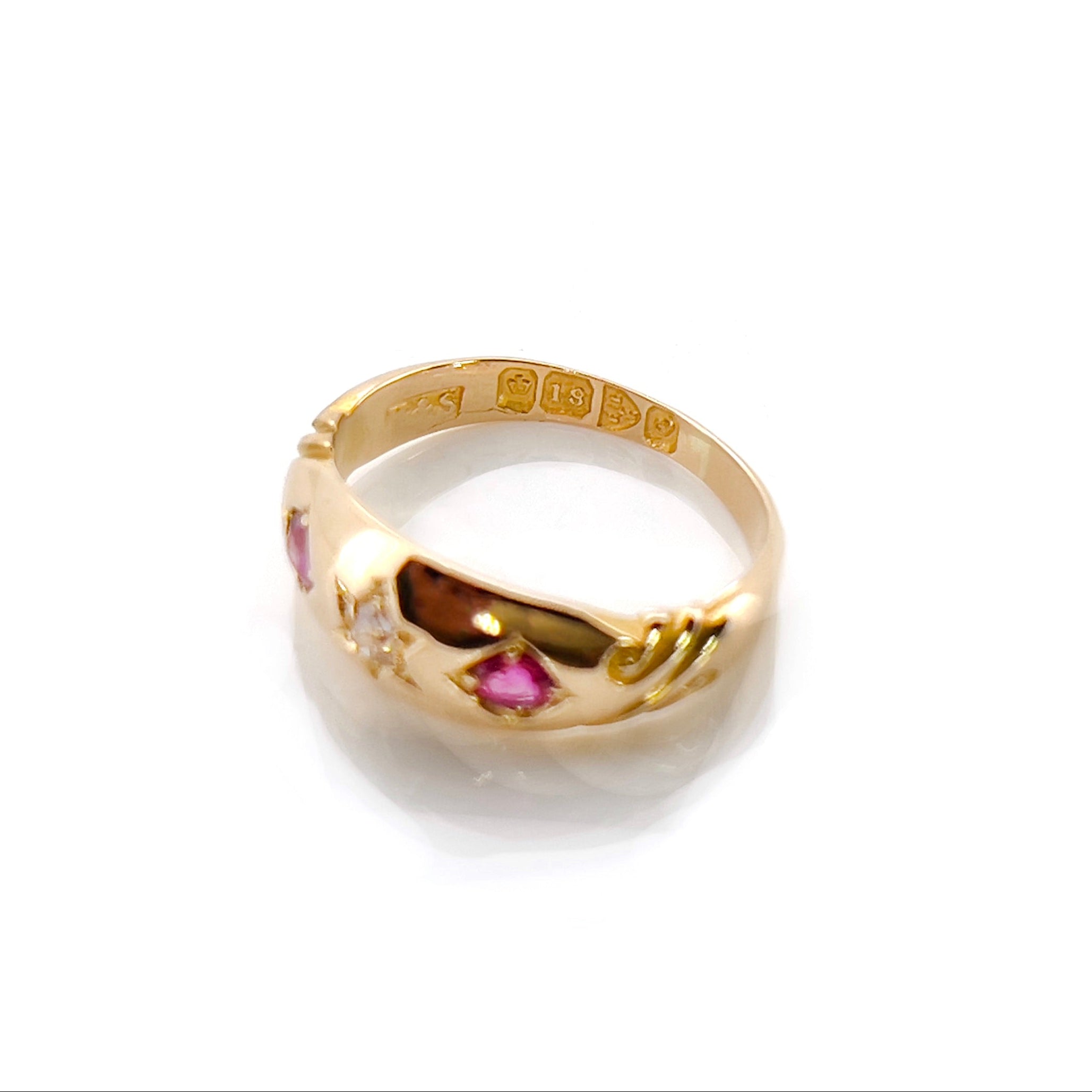 A Victorian Old Mine Cut Diamond Starburst Ring with a central diamond surrounded by two rubies, set in 18K gold with scroll work on its shoulders, and British hallmarks