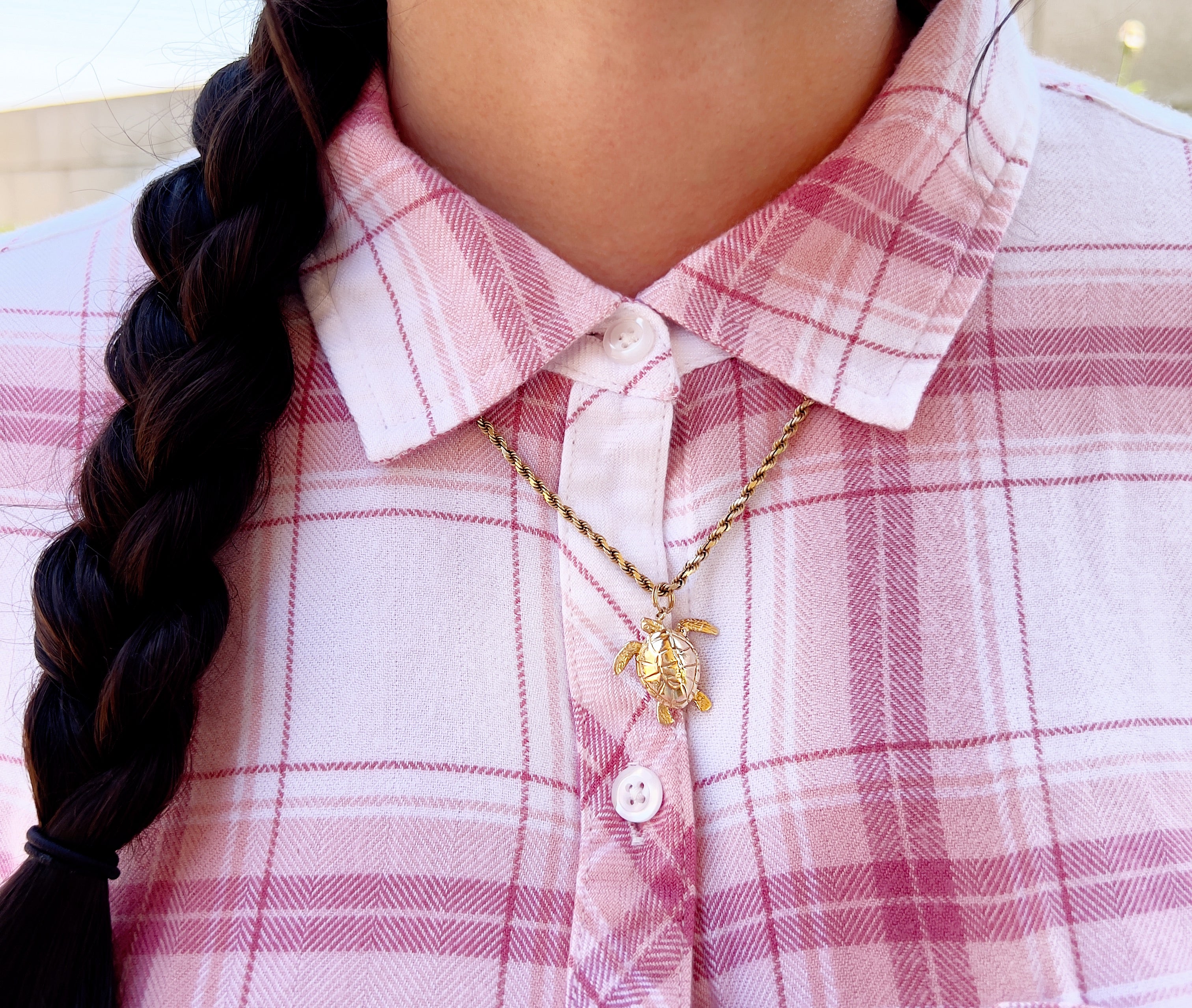 Person wearing a pink plaid shirt with a necklace featuring a turtle pendant.