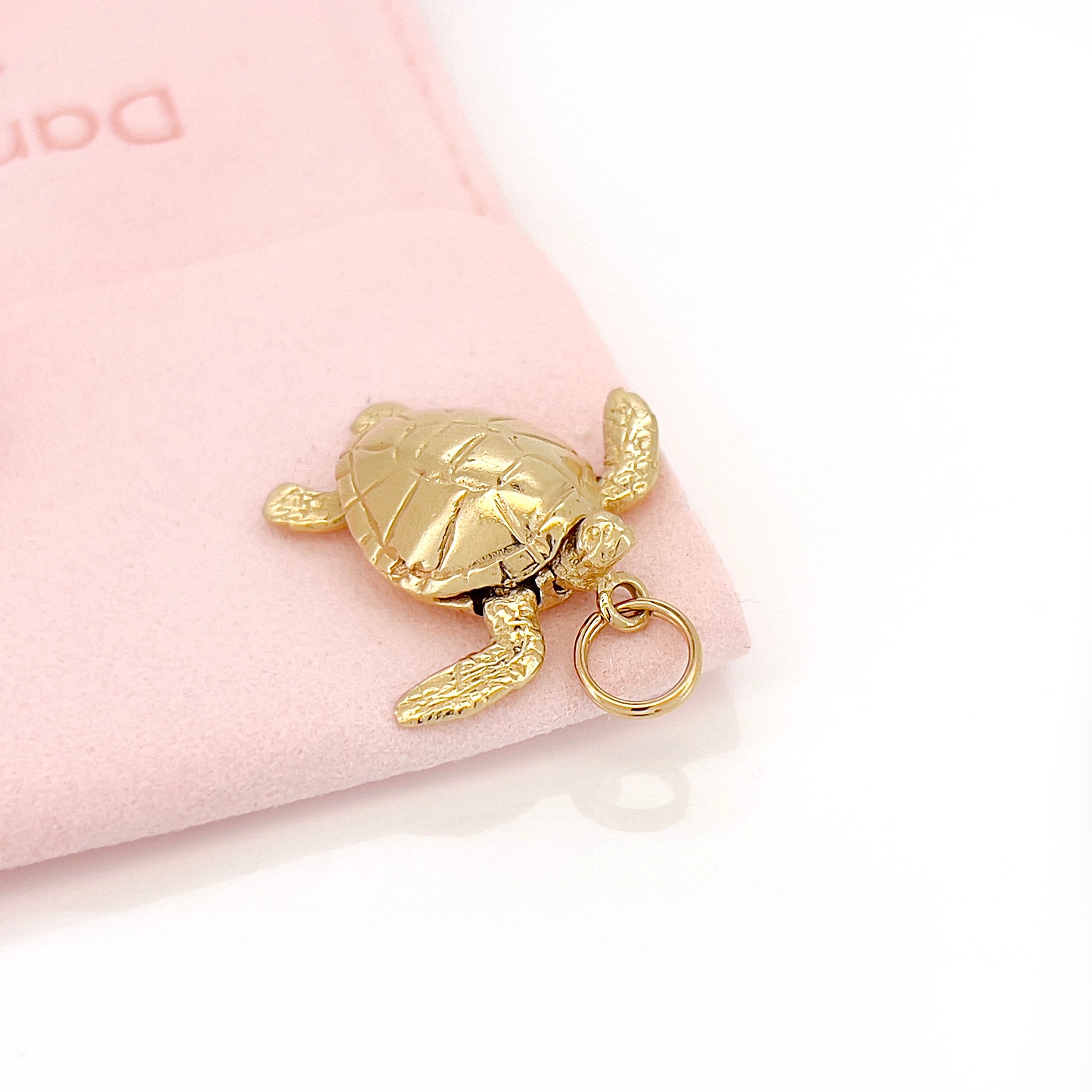 Gold turtle charm on a pink background