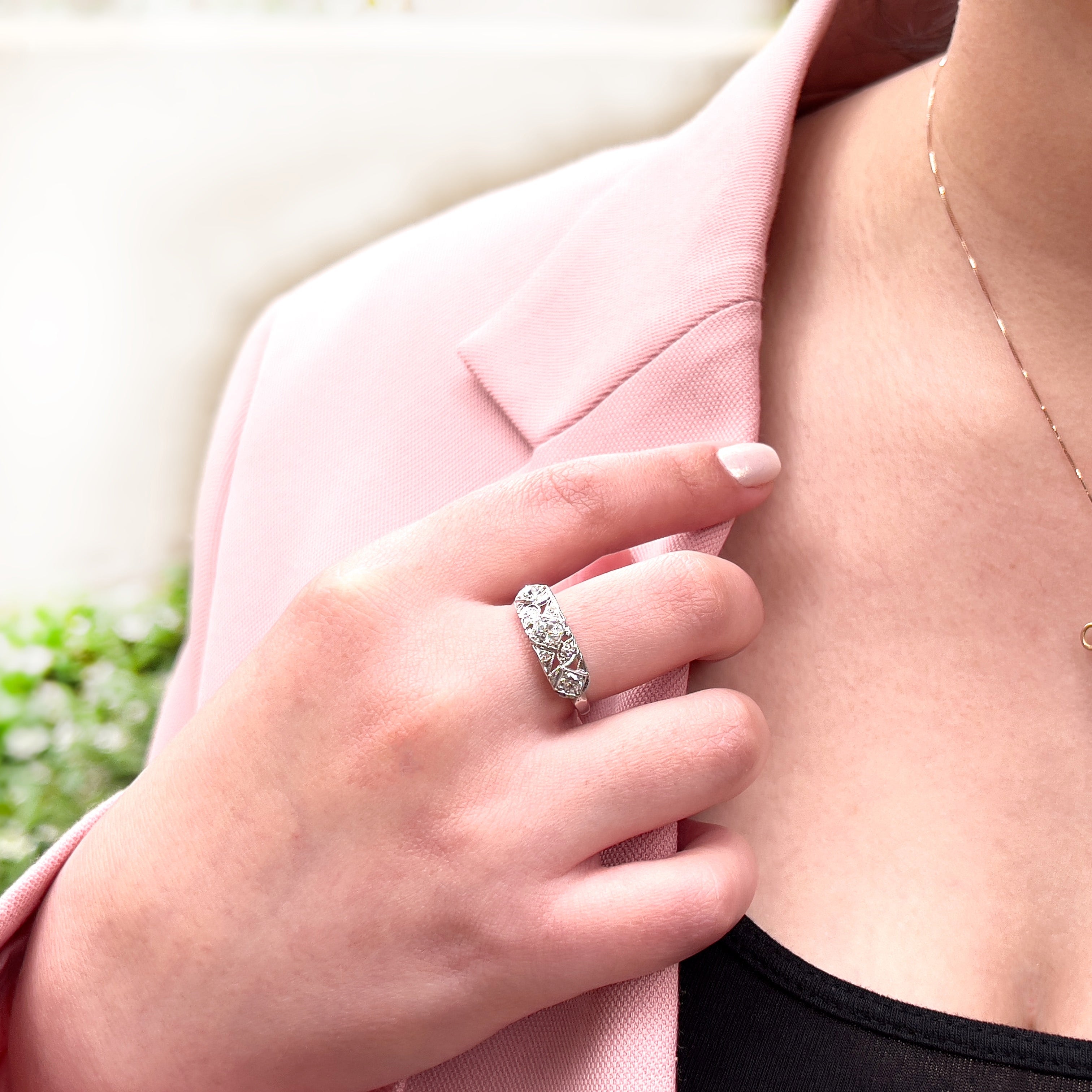 A person wearing a vintage white gold ring with a central transitional cut diamond flanked by old European cut diamonds, with intricate engraving.