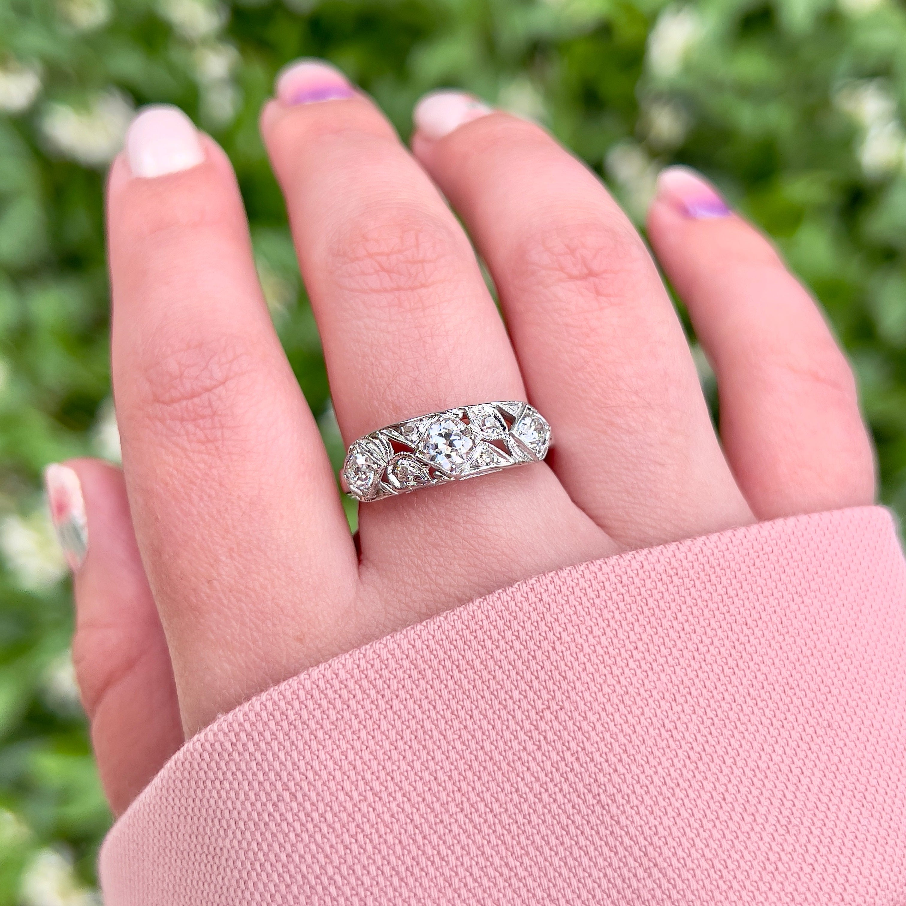 A person wearing a vintage white gold ring with a central transitional cut diamond flanked by old European cut diamonds, with intricate engraving.