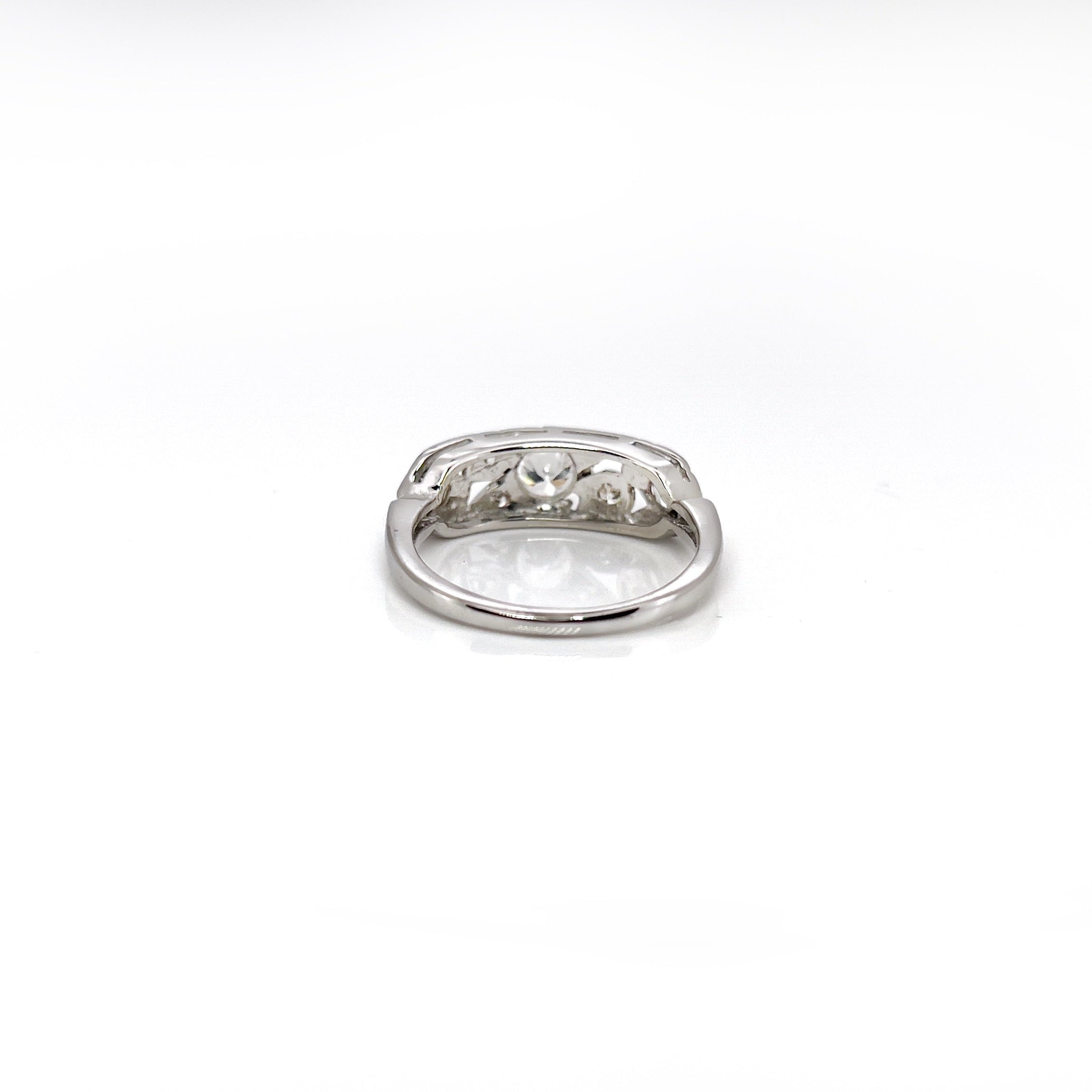 A vintage white gold ring with a central transitional cut diamond flanked by old European cut diamonds, with intricate engraving.