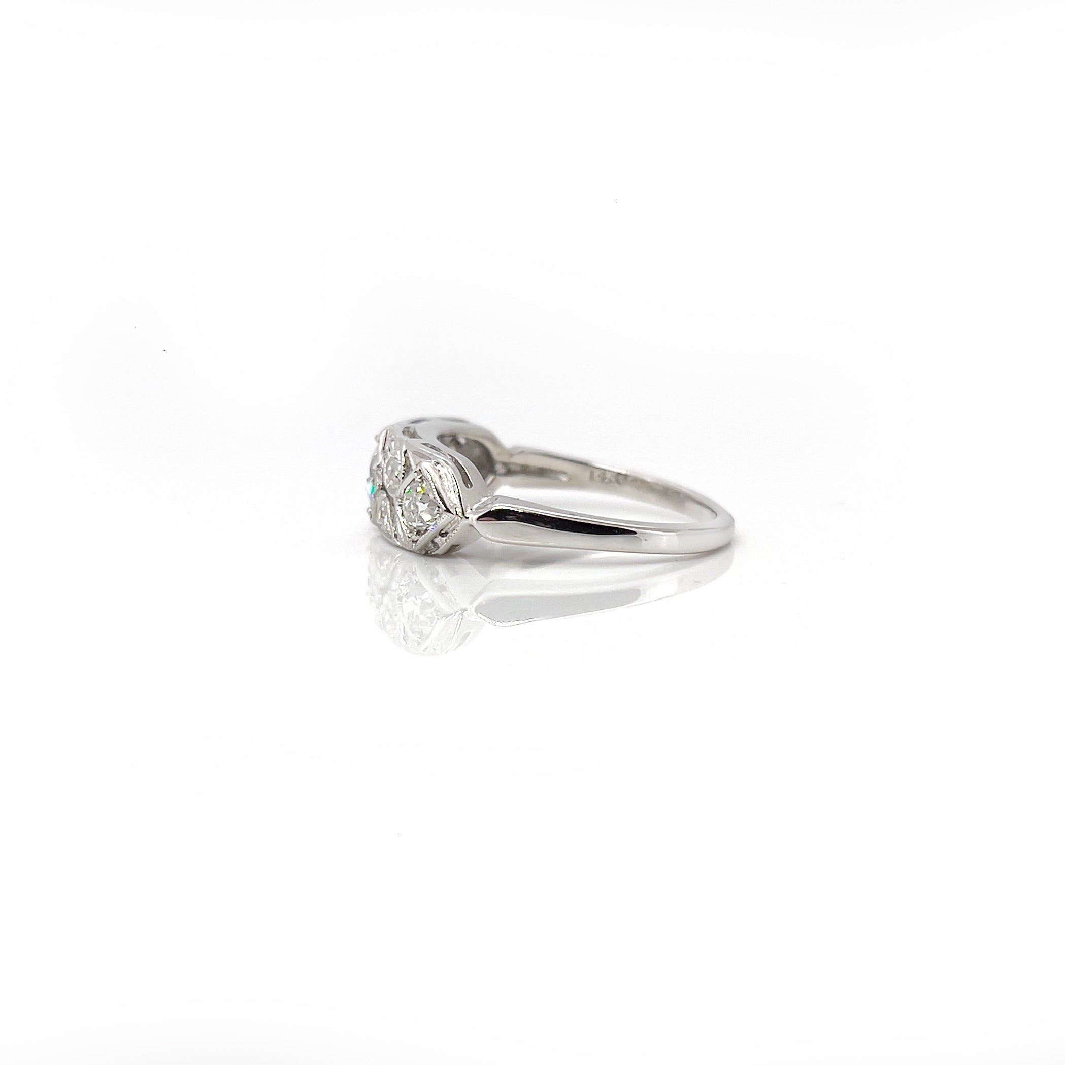 A vintage white gold ring with a central transitional cut diamond flanked by old European cut diamonds, with intricate engraving.