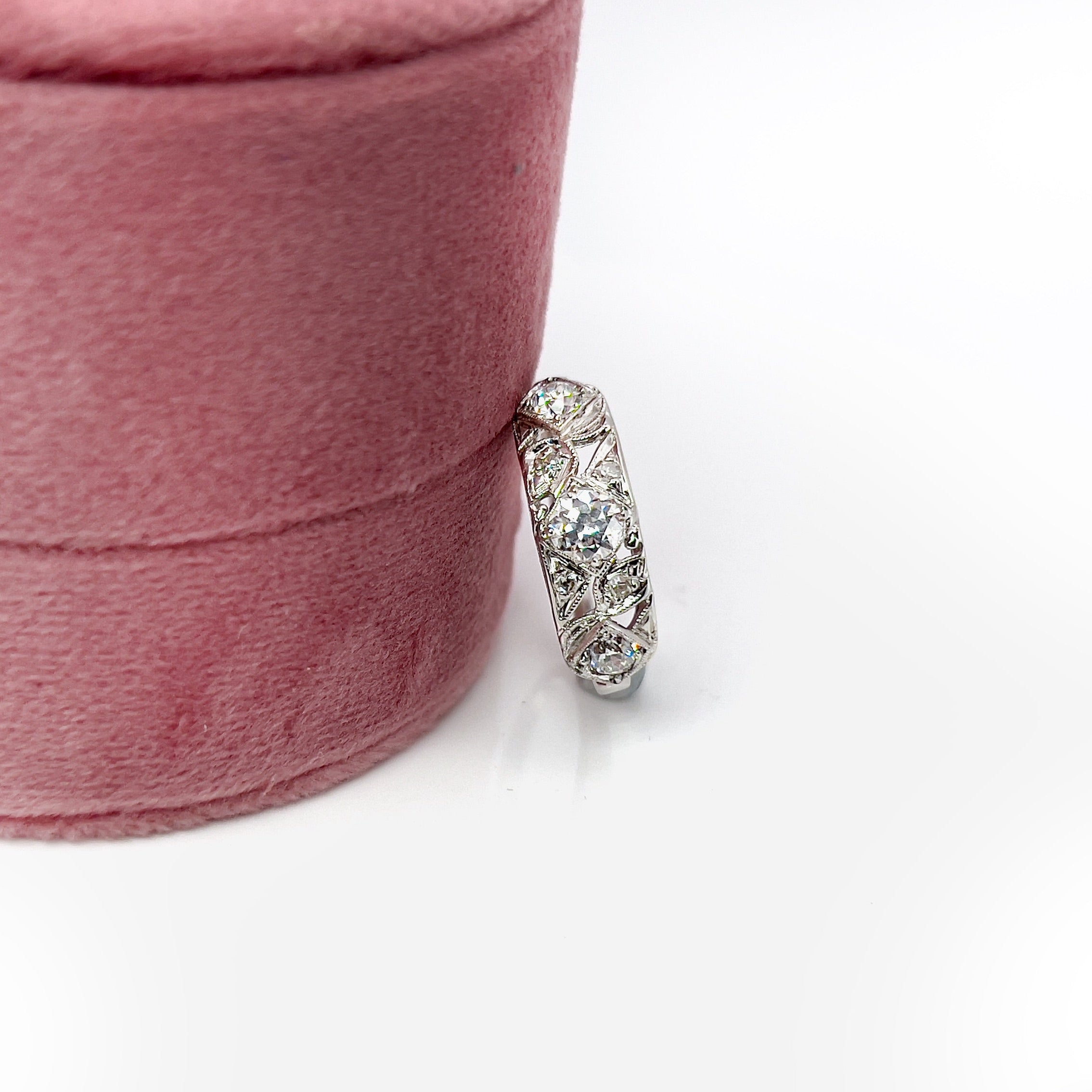 A vintage white gold ring with a central transitional cut diamond flanked by old European cut diamonds, with intricate engraving.