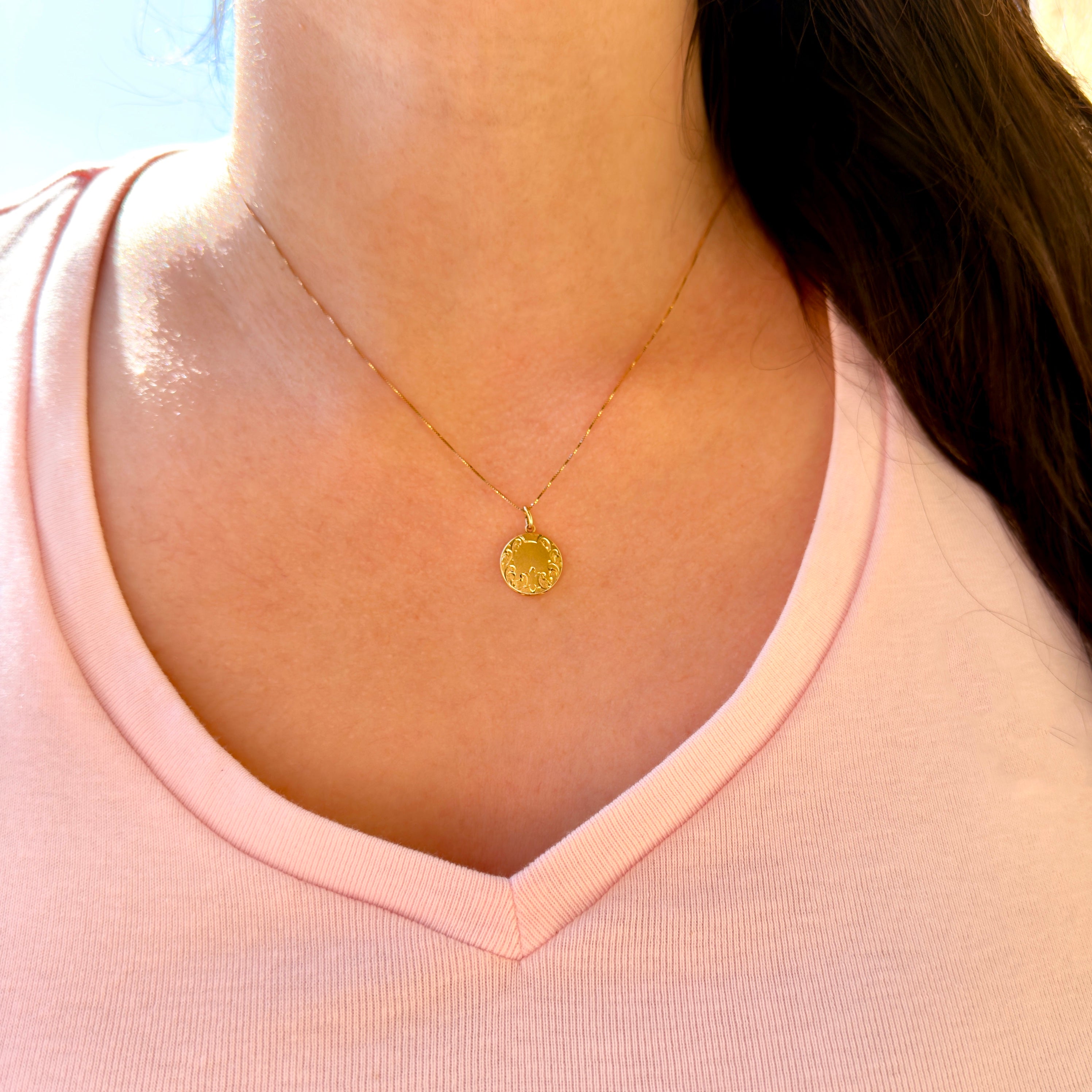 Gold necklace with a pendant worn by a person in a pink shirt.