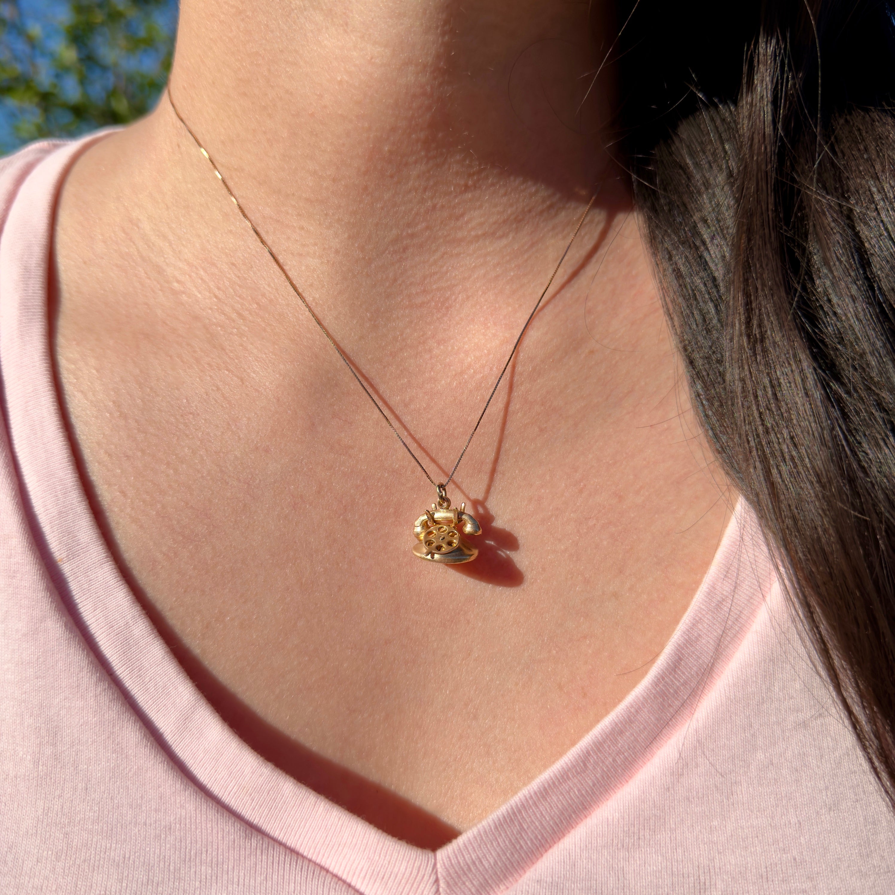 Person wearing a gold necklace with a pendant, outdoors.