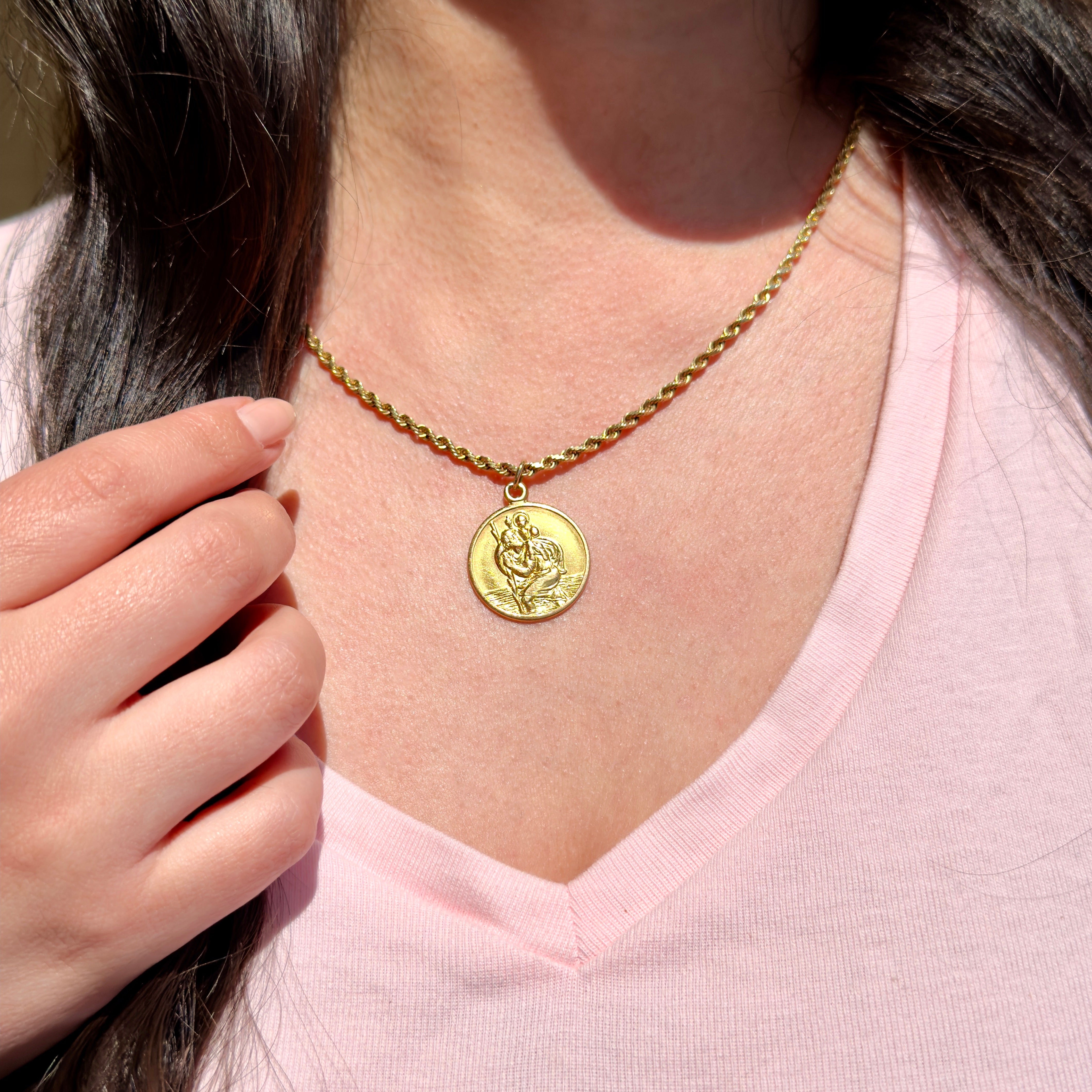 Gold necklace with a round pendant worn by a person in a pink shirt.