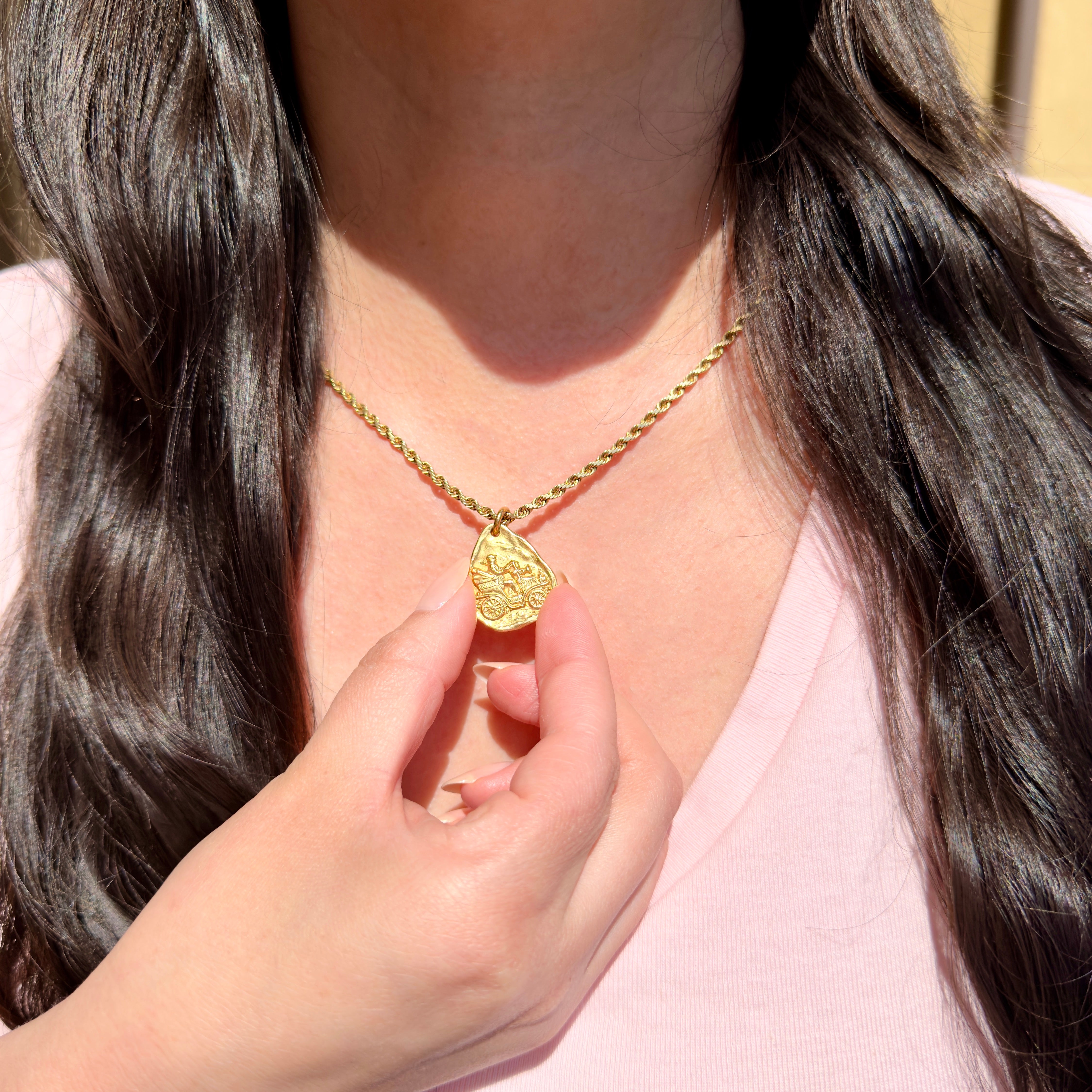Person wearing a gold necklace with a pendant, held by a hand.