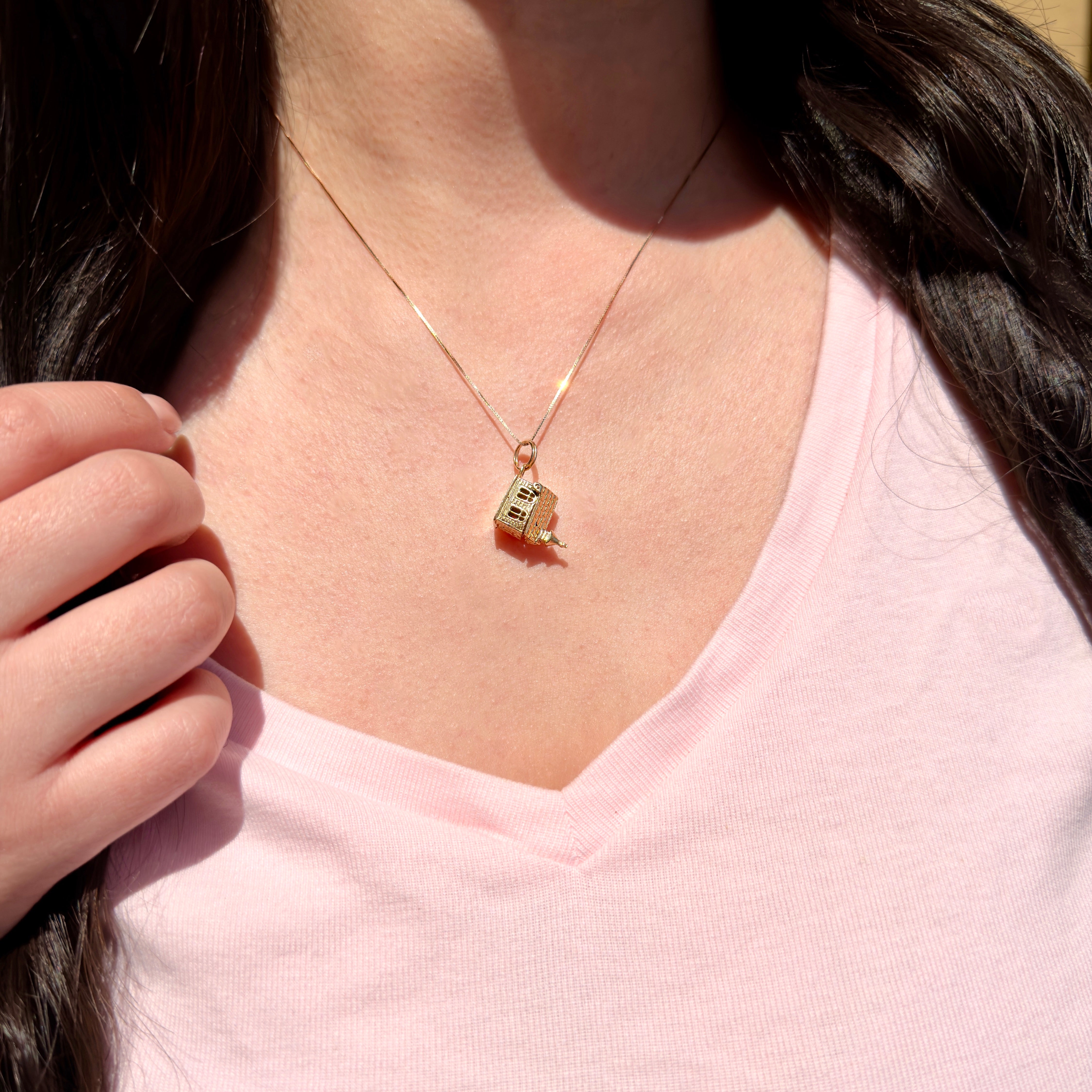 Person wearing a gold necklace with a small chapel charm, against a neutral background