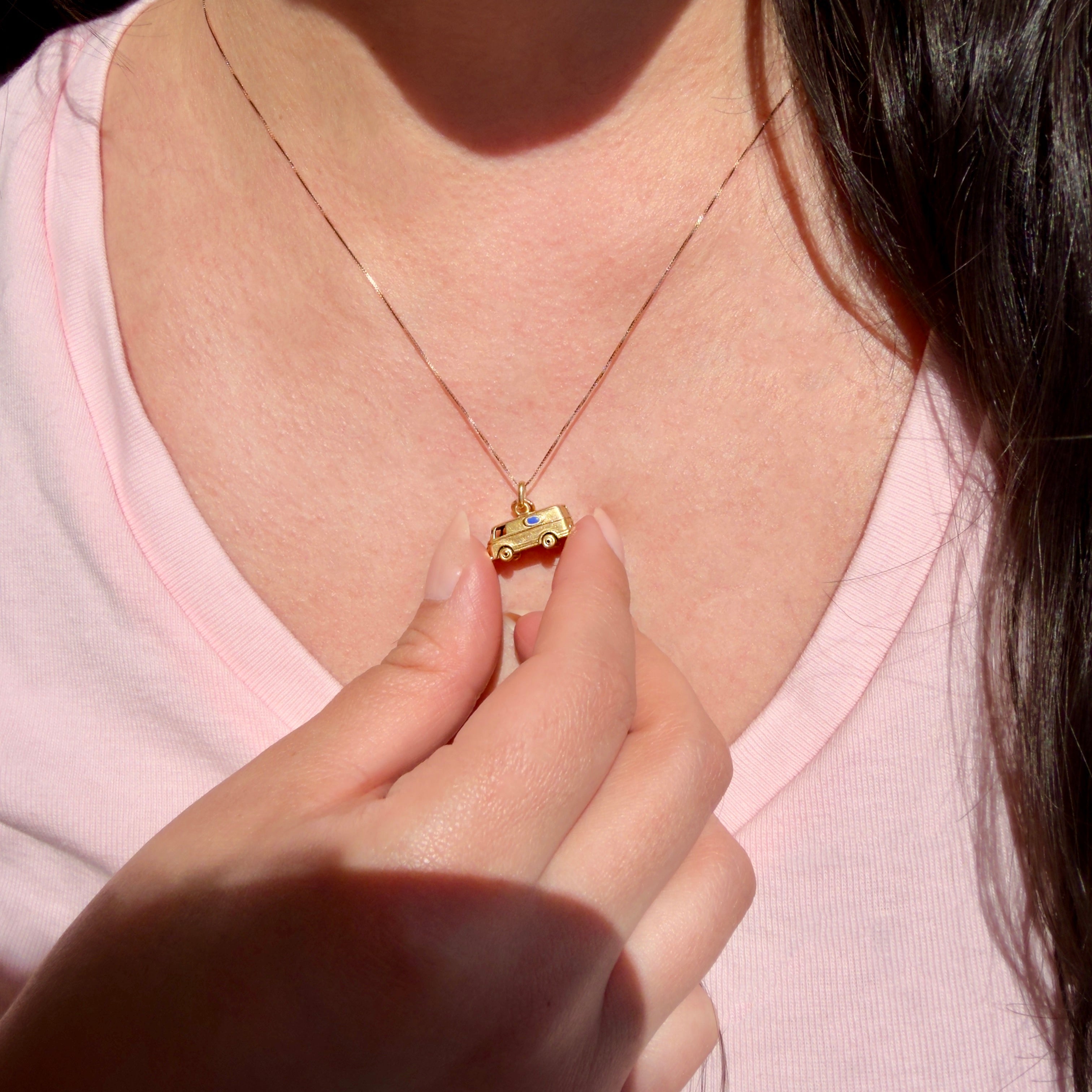 Person wearing a gold necklace with a small microbus charm on a pink shirt.