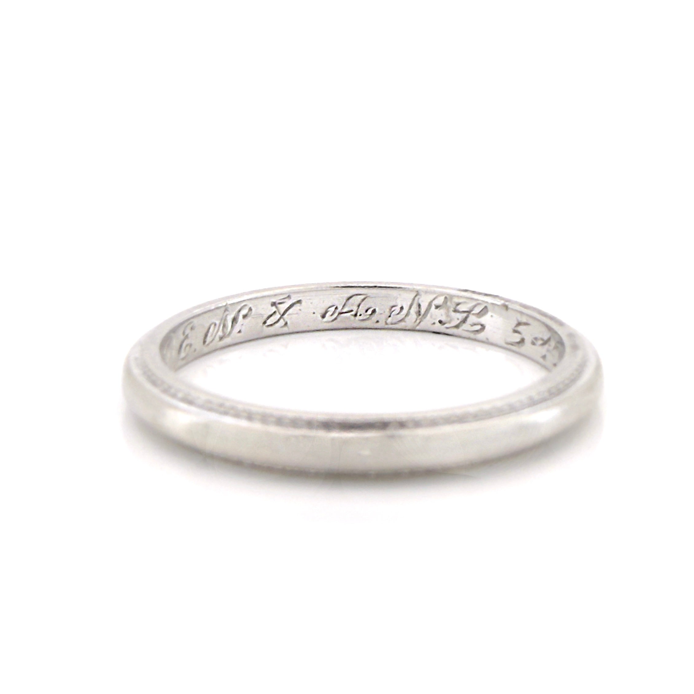Vintage platinum ring with engraved text on a white background