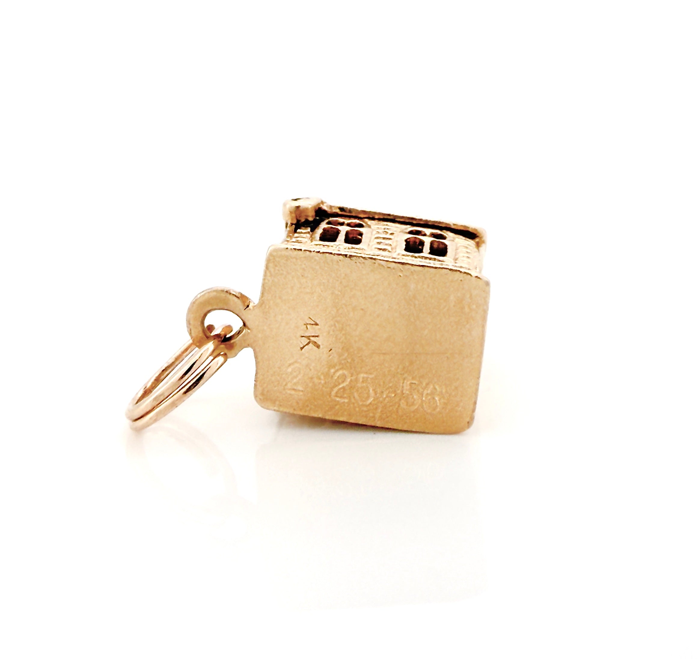 Bottom of a vintage gold miniature chapel charm with a '2-25-56' inscription on a white background