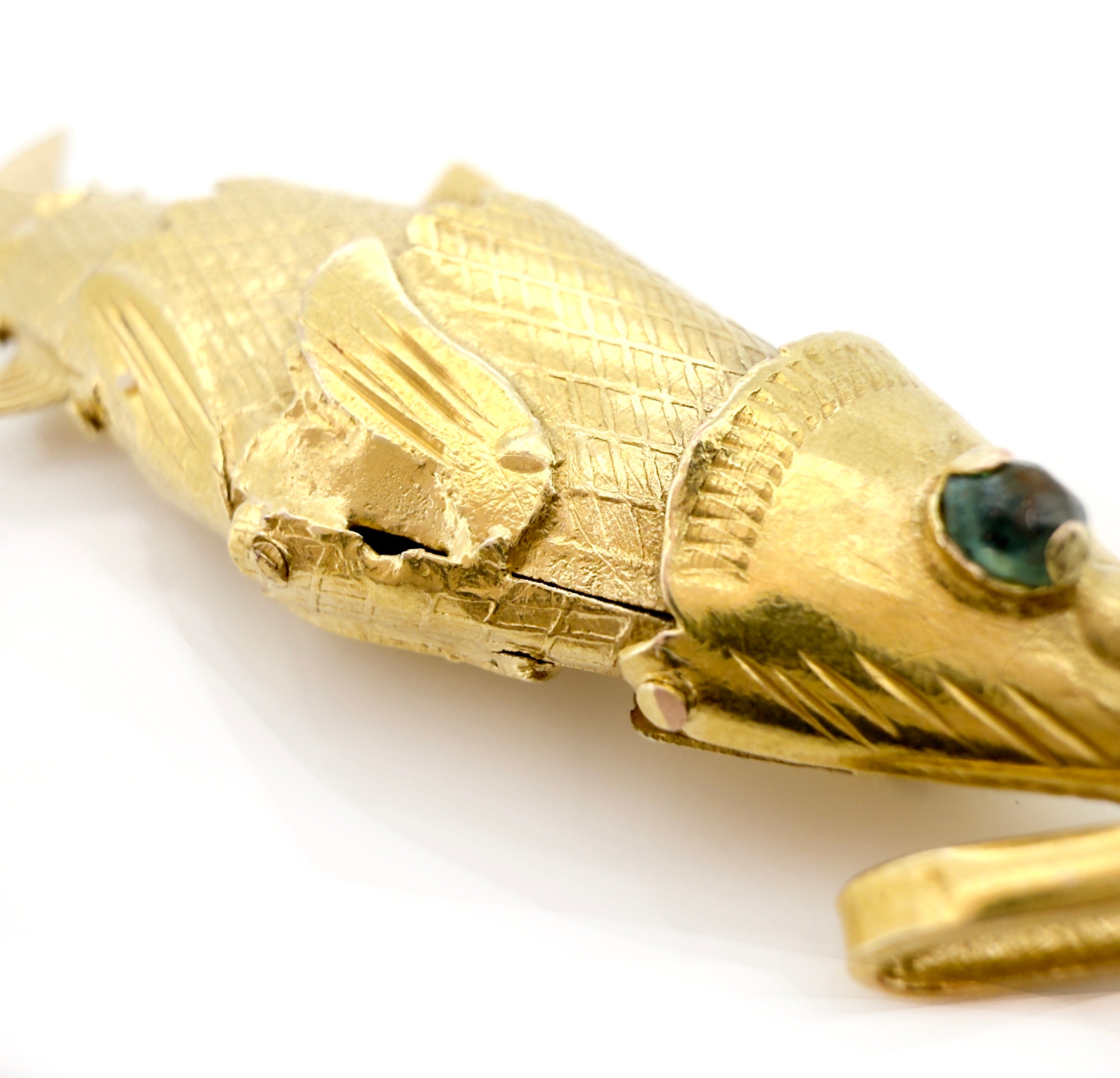 Gold snake-shaped object with a green stone on a white background