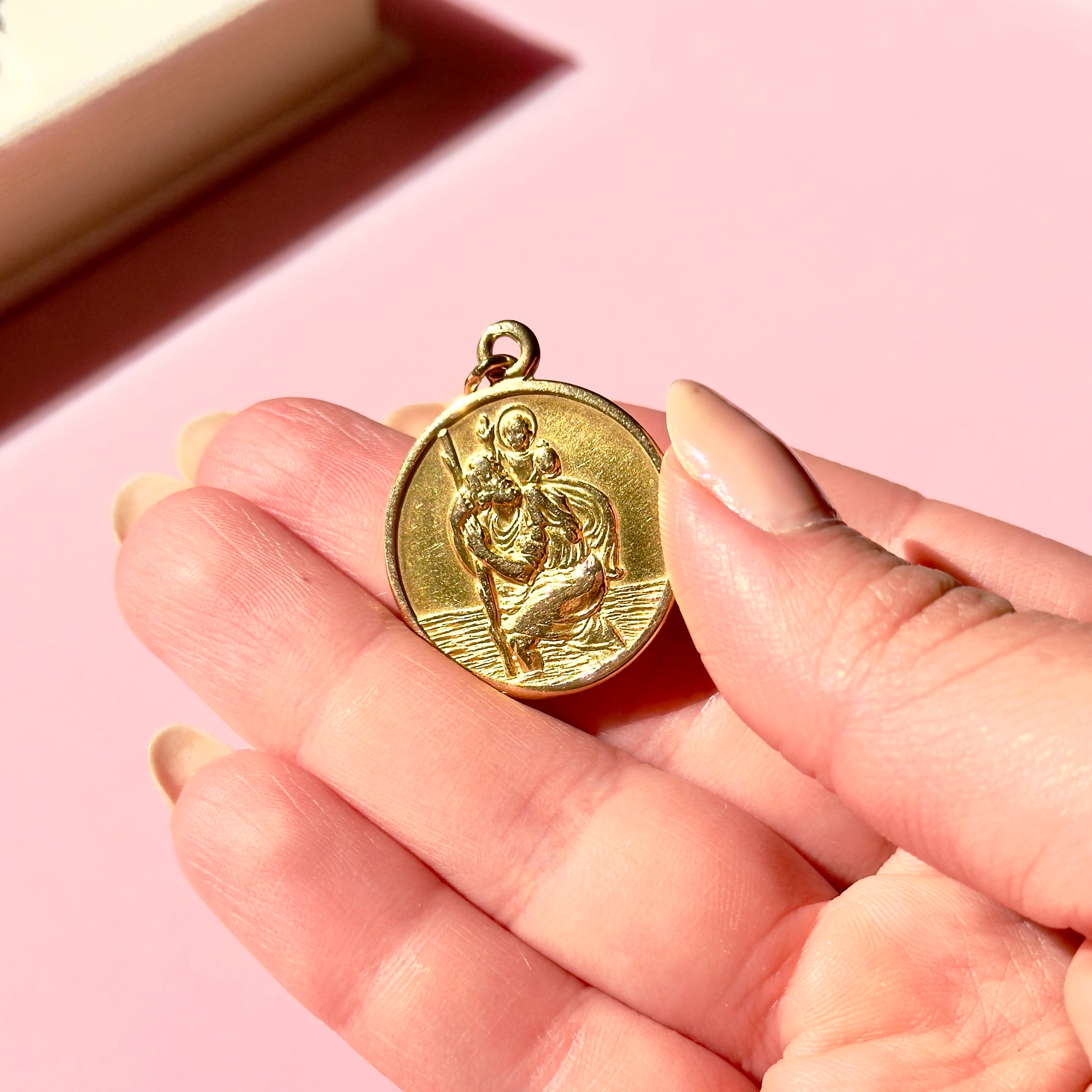 Vintage gold pendant held in a hand against a pink background