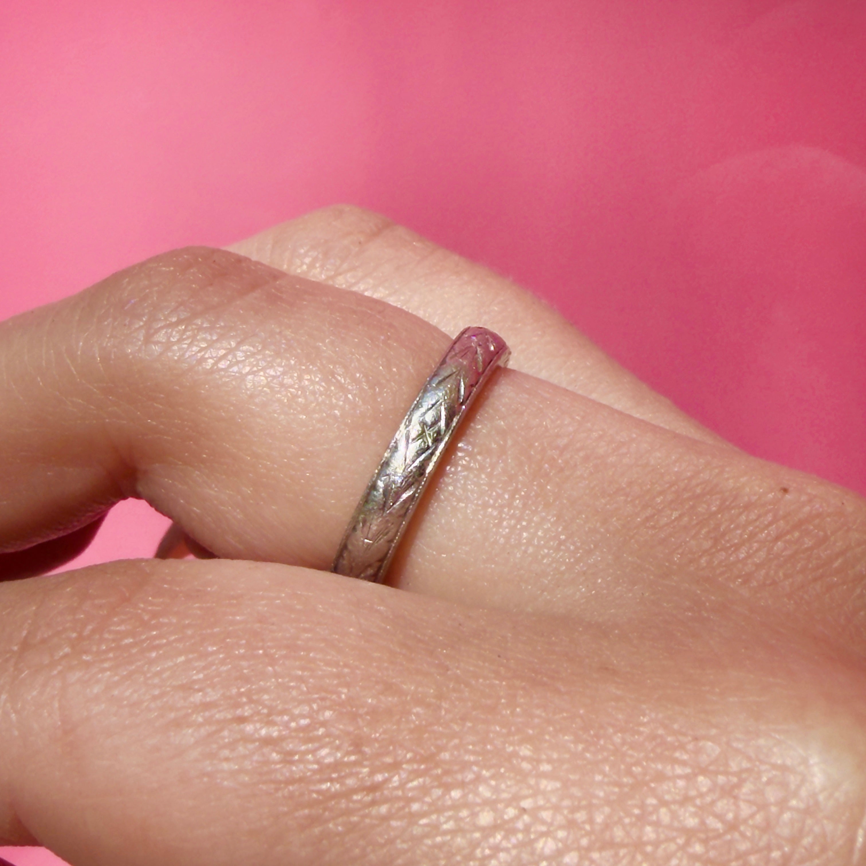 Vintage platinum ring on a finger against a pink background