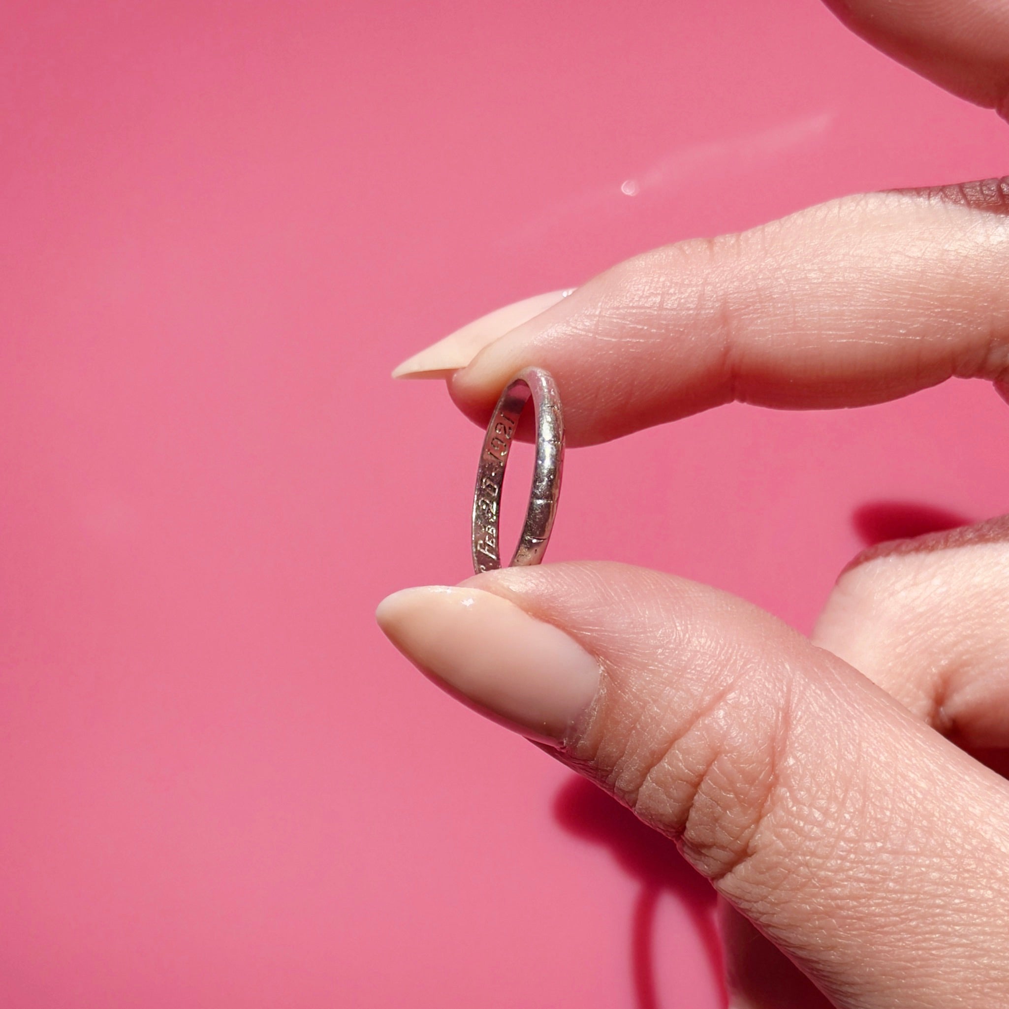 Hand holding an antique platinum ring against a pink background