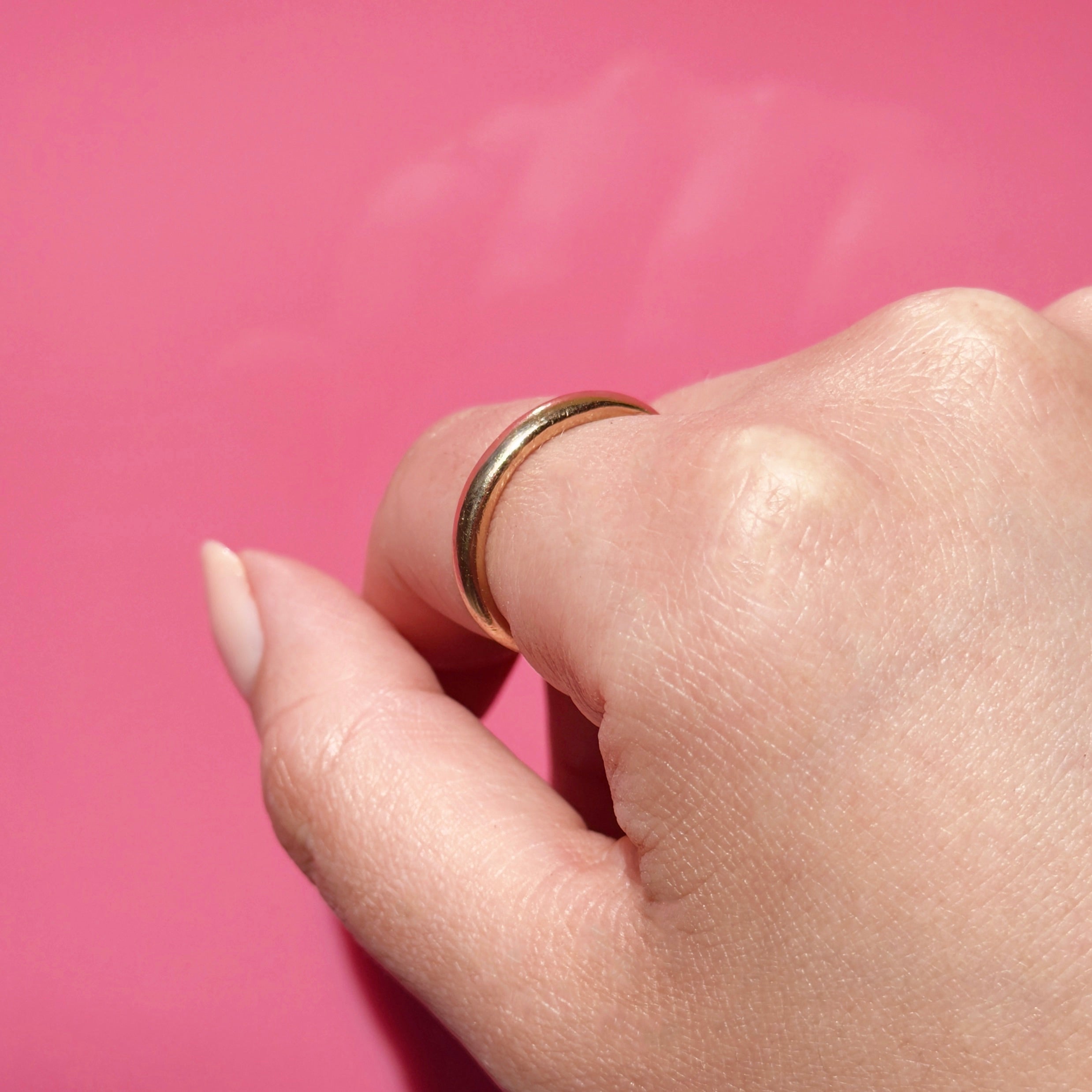 Antique gold ring on a person's finger against a pink background