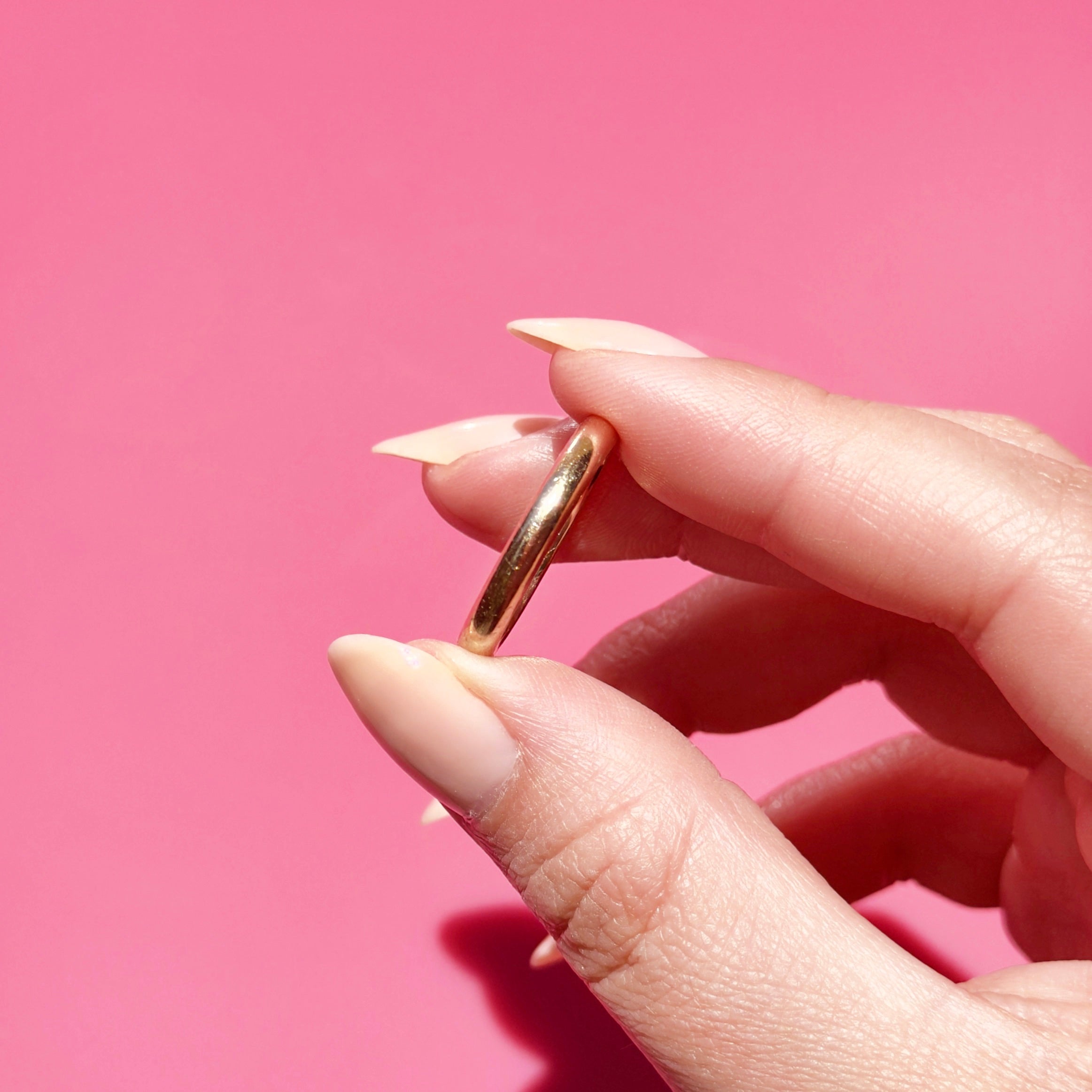 Antique gold ring held between fingers against a pink background