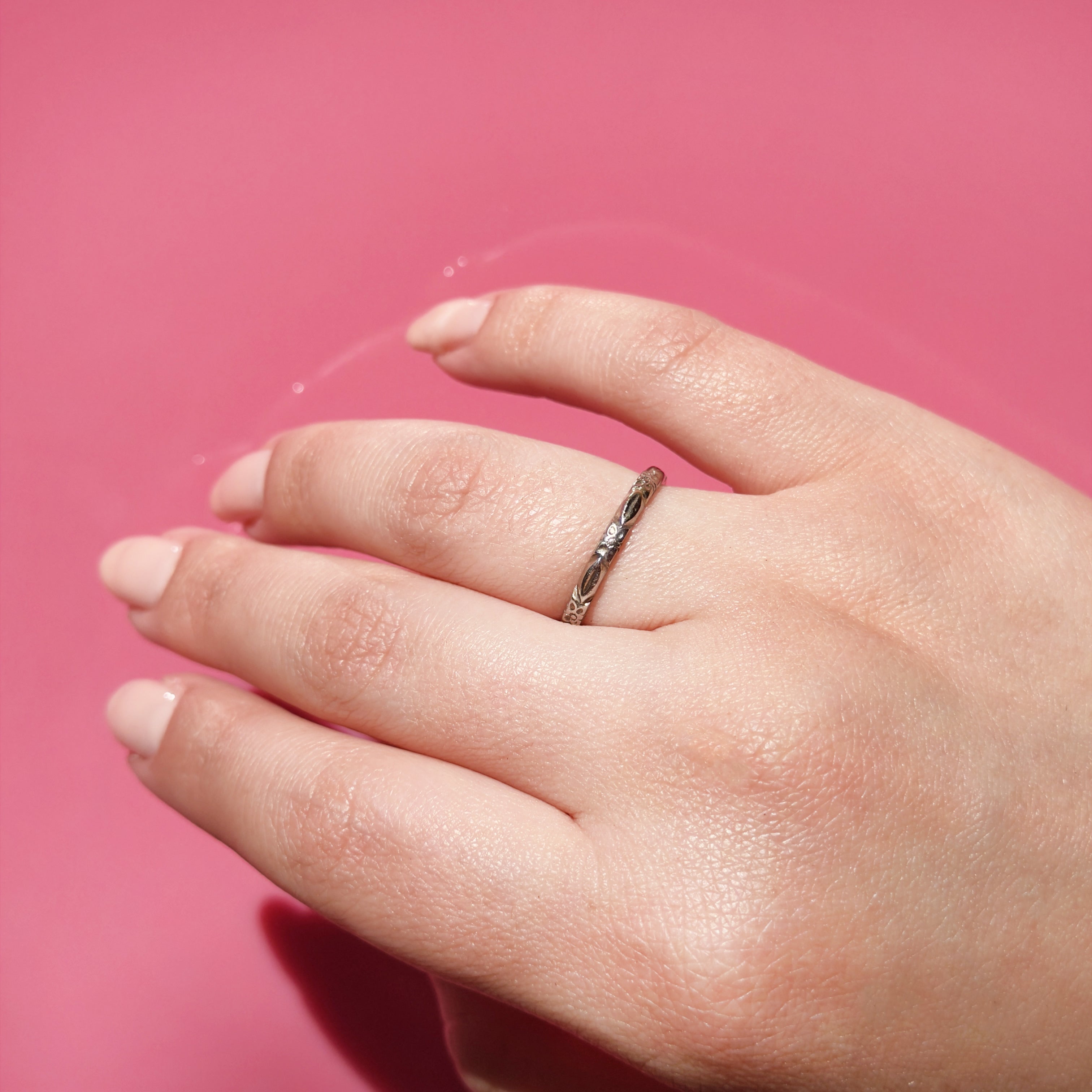 Hand wearing a white gold ring with a flower pattern on a pink background