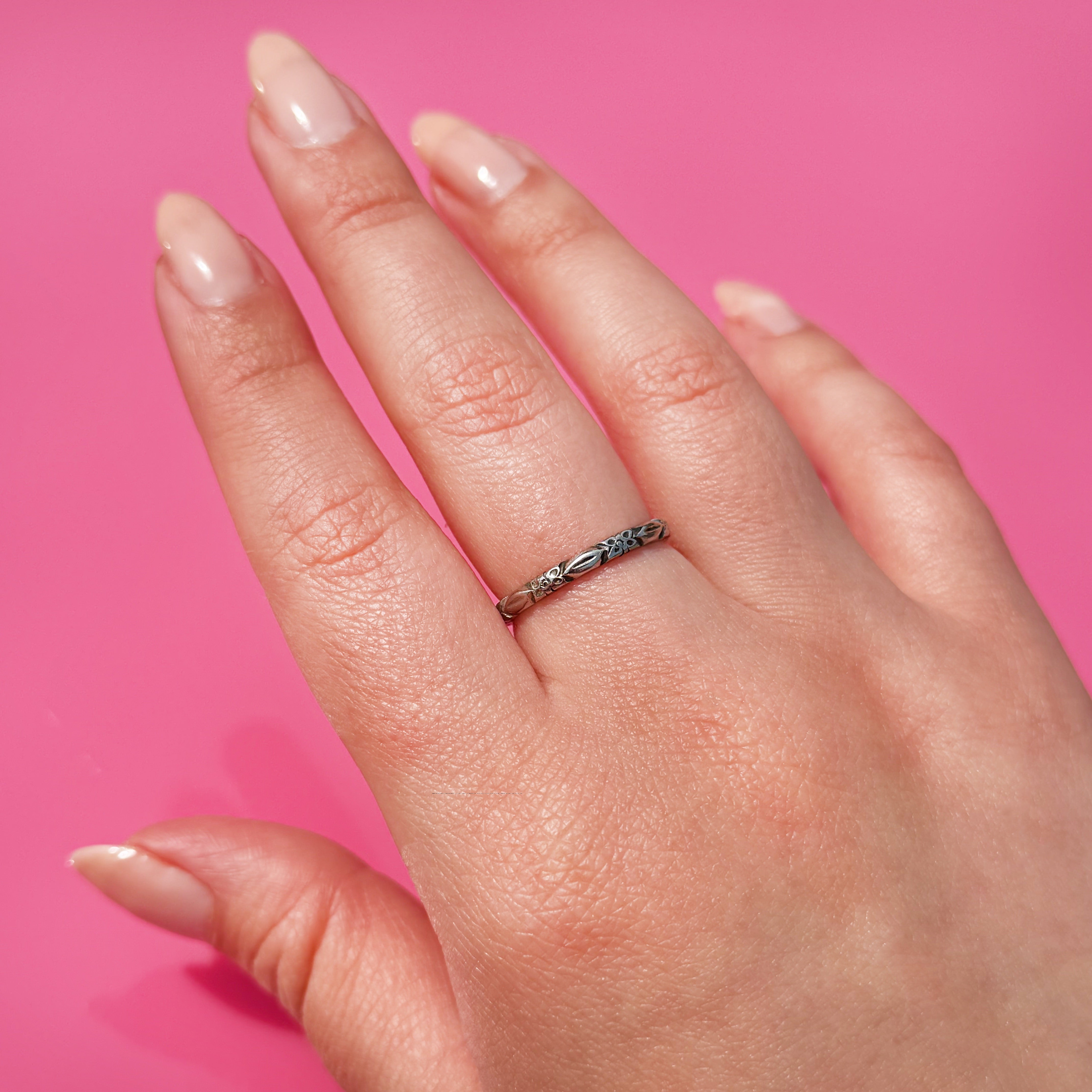 Hand wearing a white gold ring with a flower pattern on a pink background