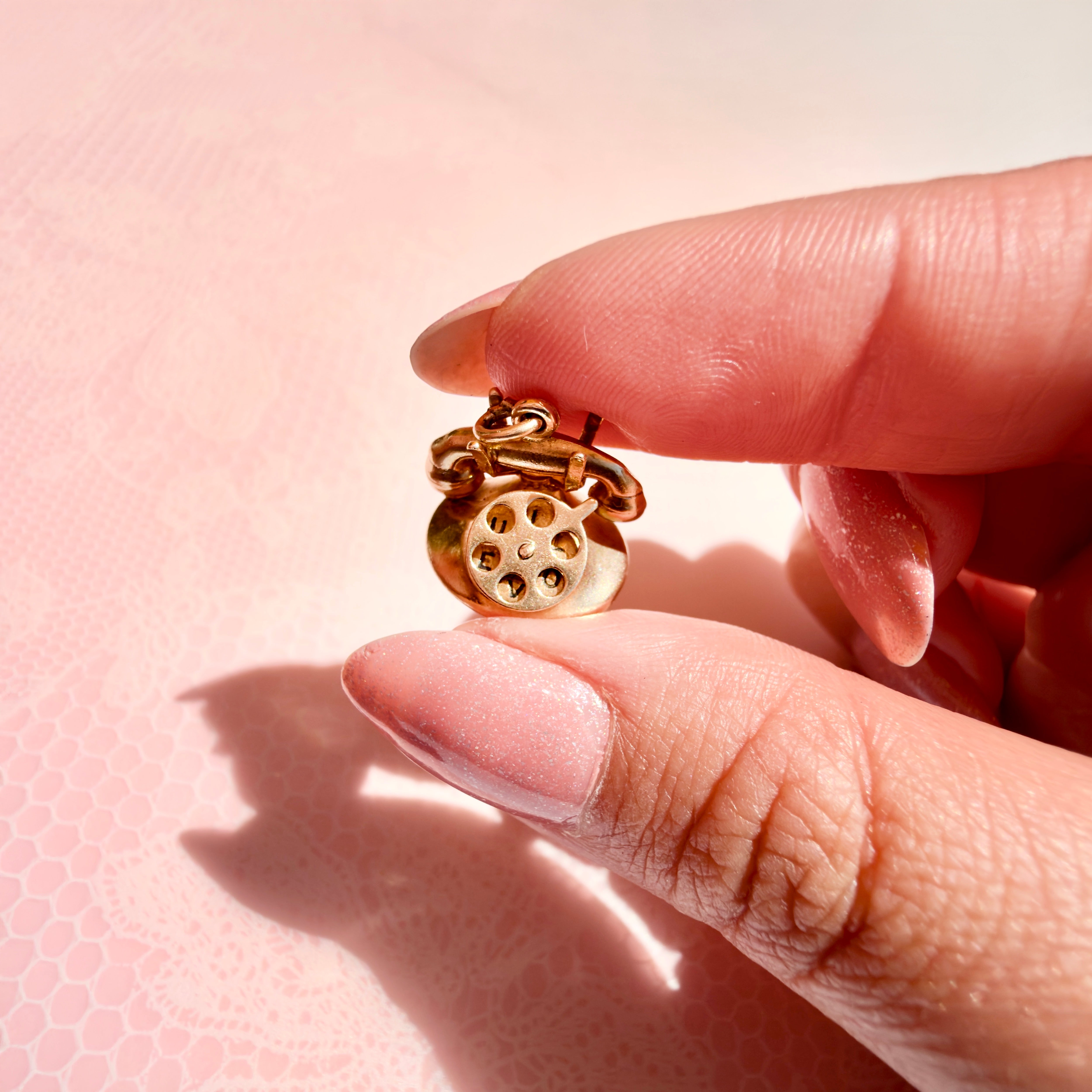 A hand holding a vintage gold charm against a pink background