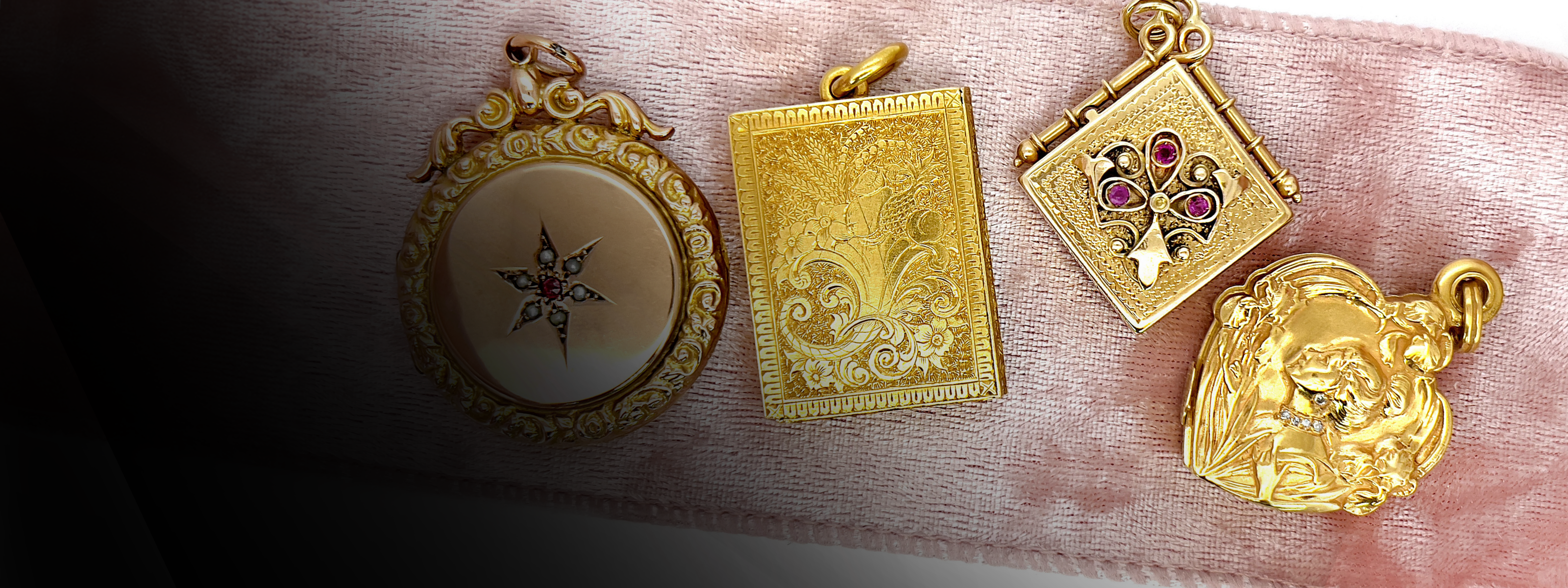 Four gold antique lockets displayed on a pink velvet ribbon against a white background with a dark gradient at the bottom. 