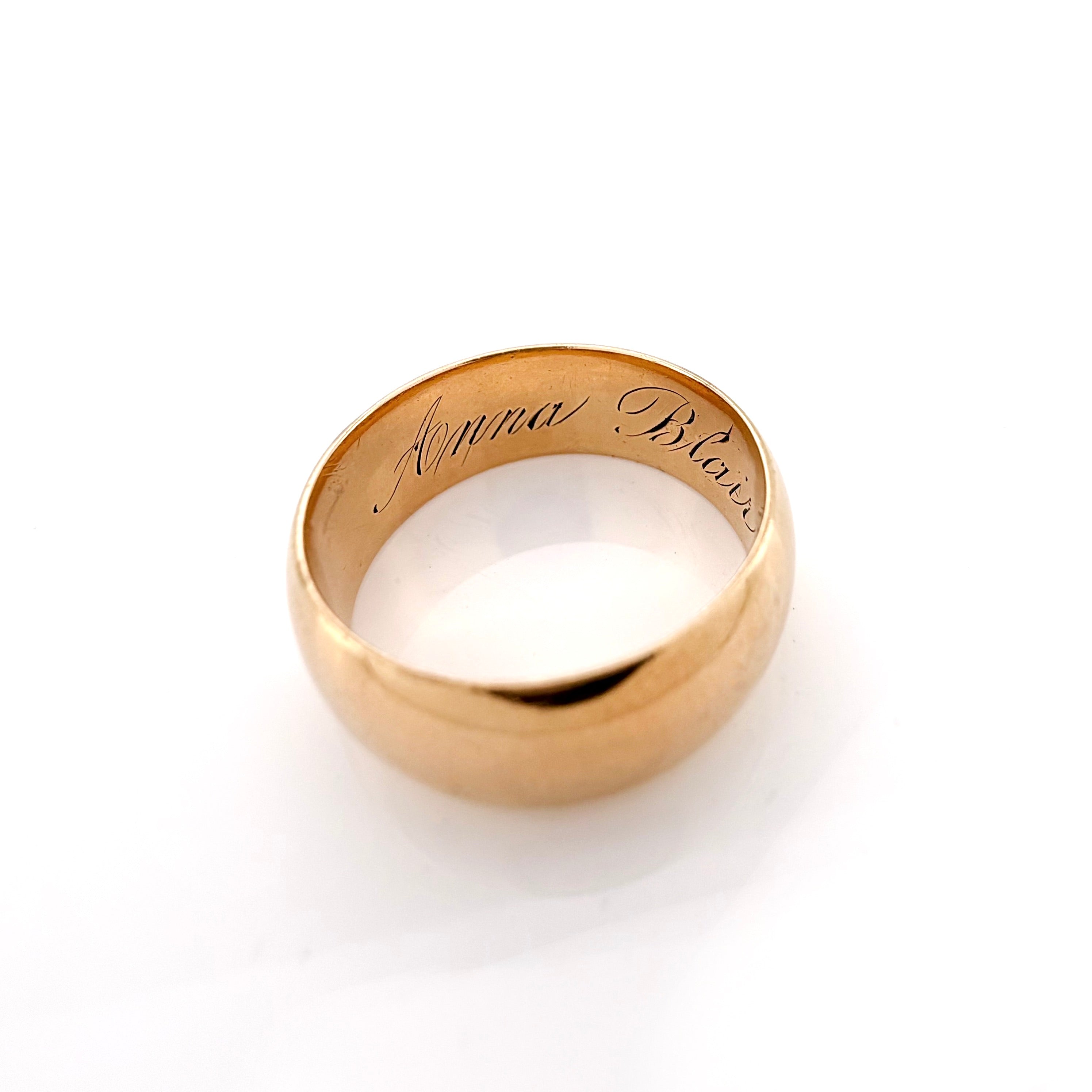 A gold band ring with the names 'Anna Blair' engraved on the inside, shown on a clean white background.