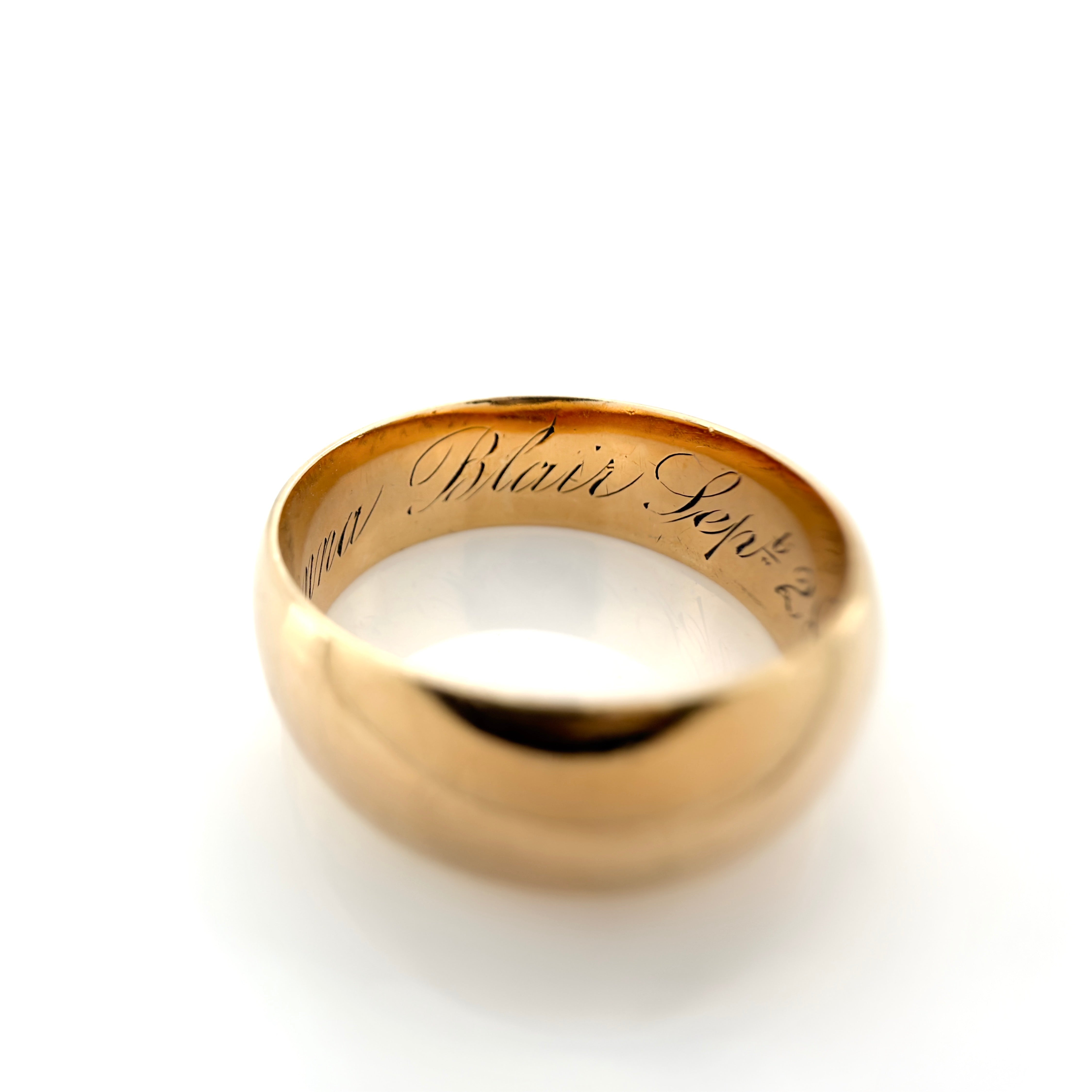 A gold band ring with the names 'Anna Blair' engraved on the inside, shown on a clean white background.