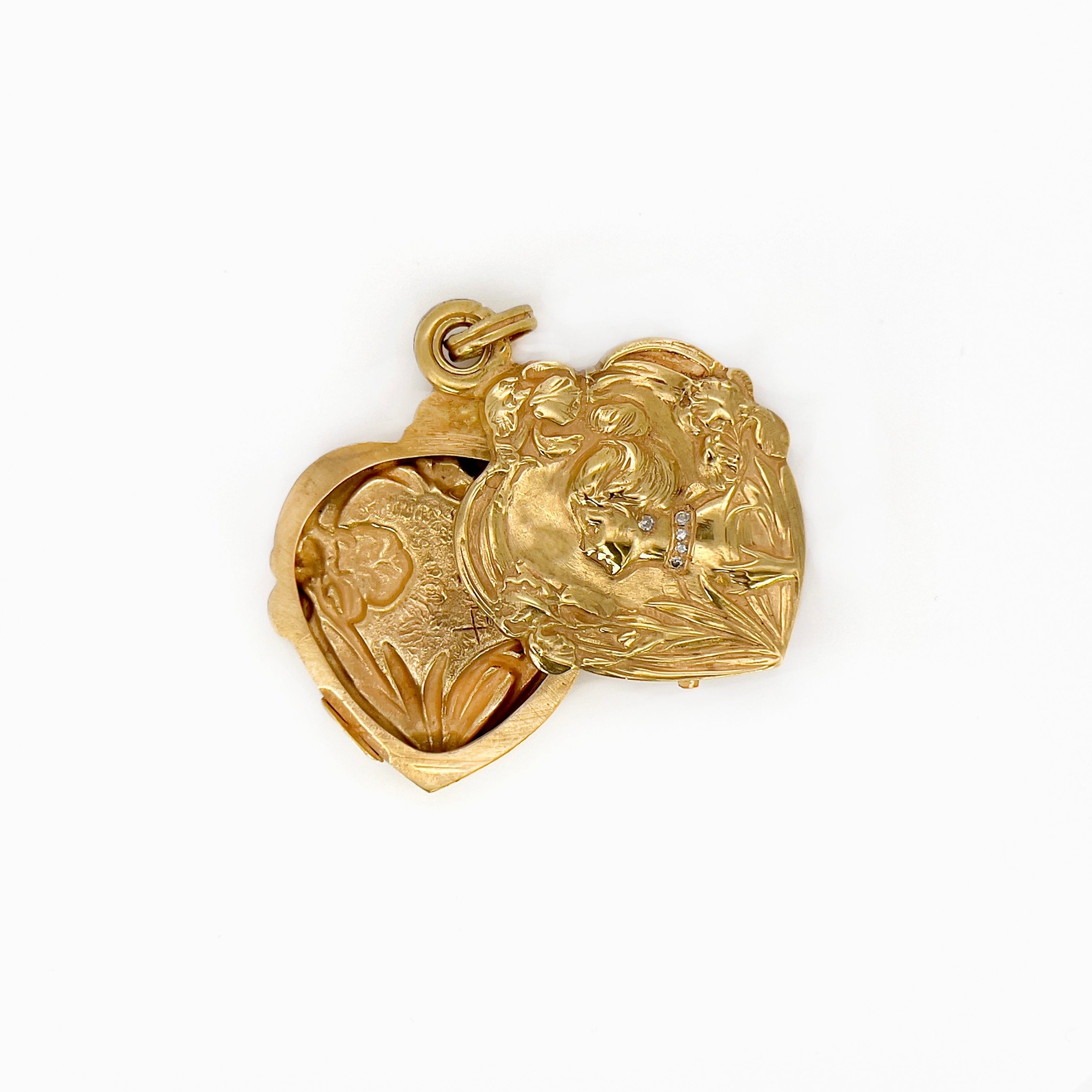 An open view of an Art Nouveau heart-shaped locket with gold detailing, featuring a central figure with a bun and flowers on the front, on a white background