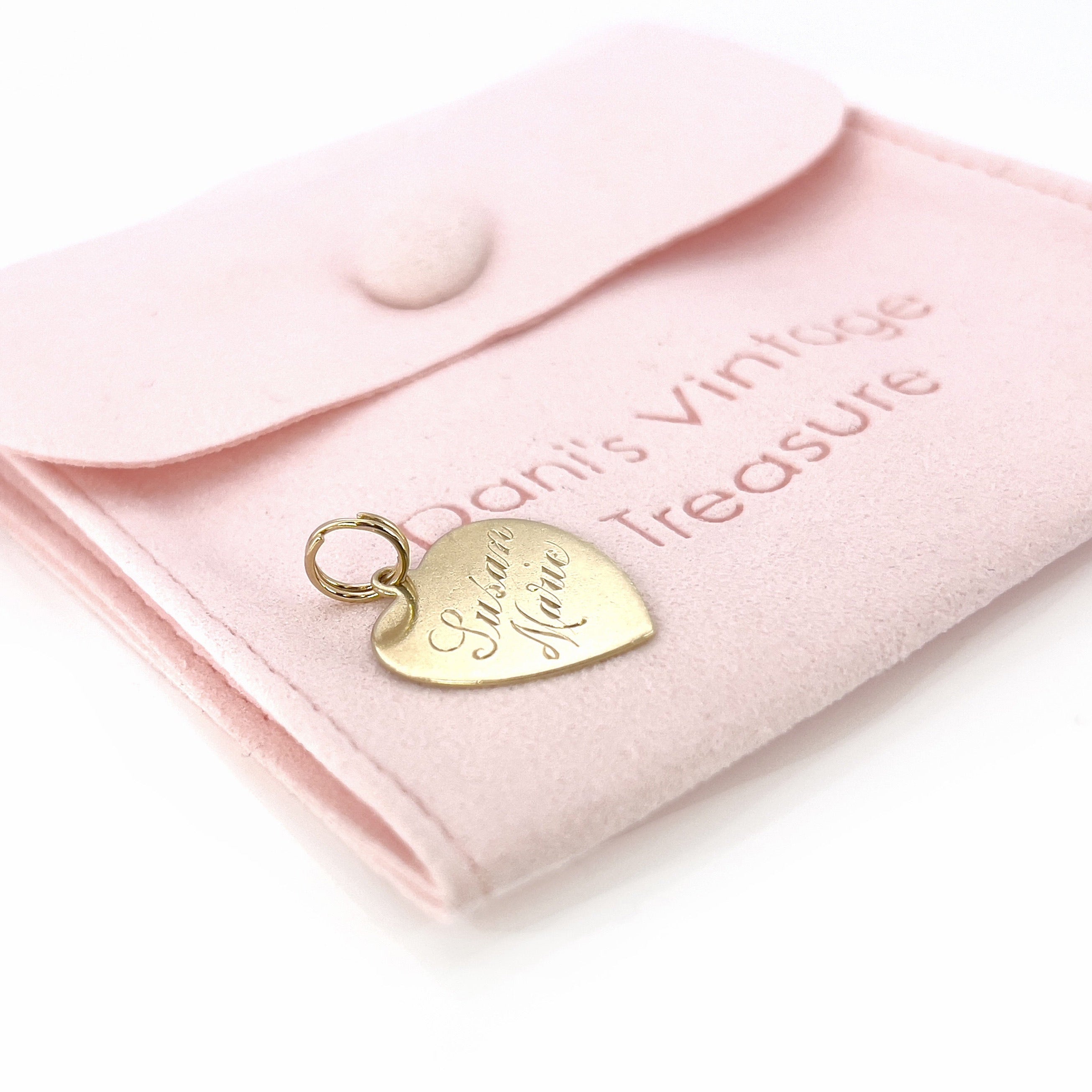 A vintage gold heart-shaped charm with the inscription 'Susan Marie' on a pink pouch. 
