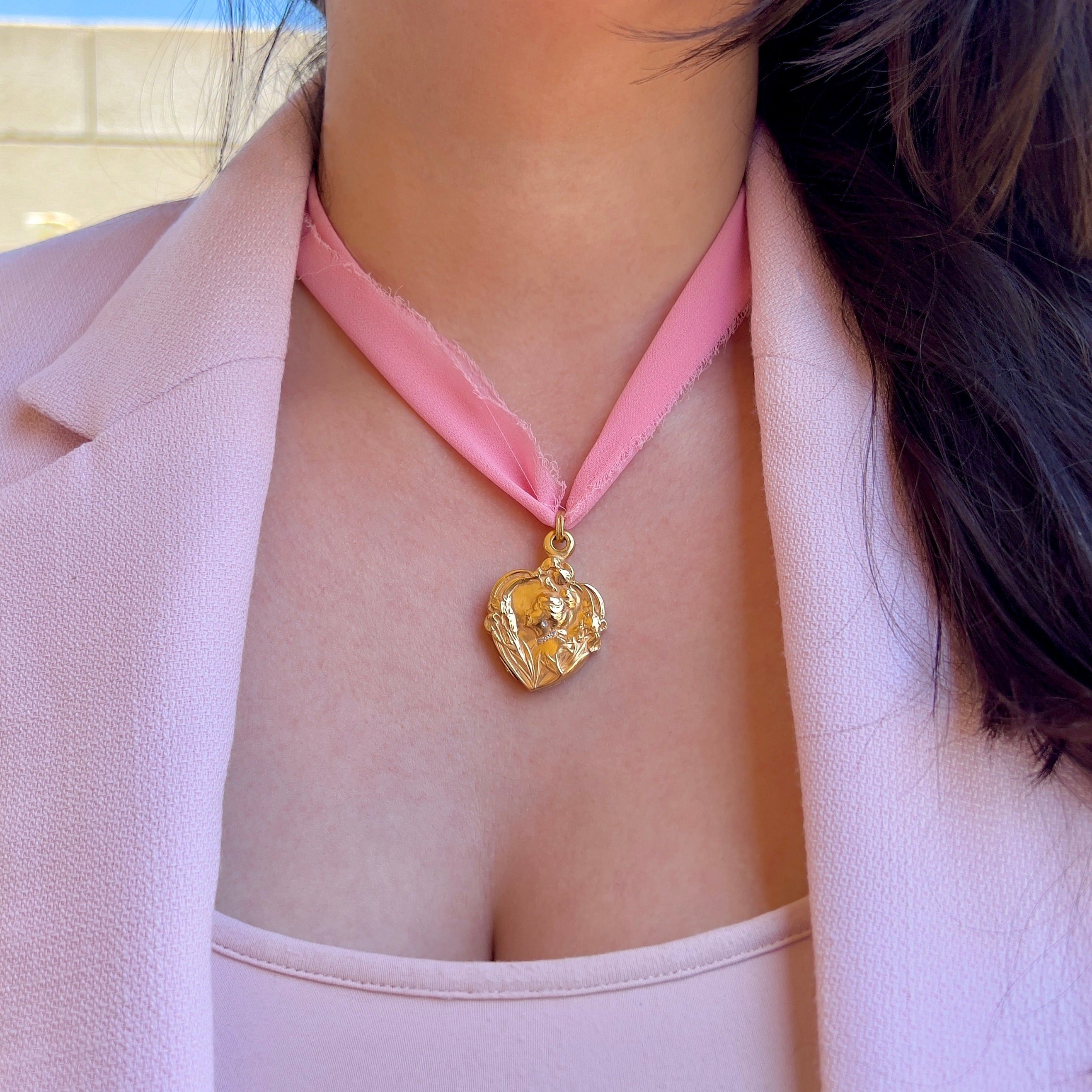 A close up of a person wearing a pink ribbon with an Art Nouveau gold locket. 