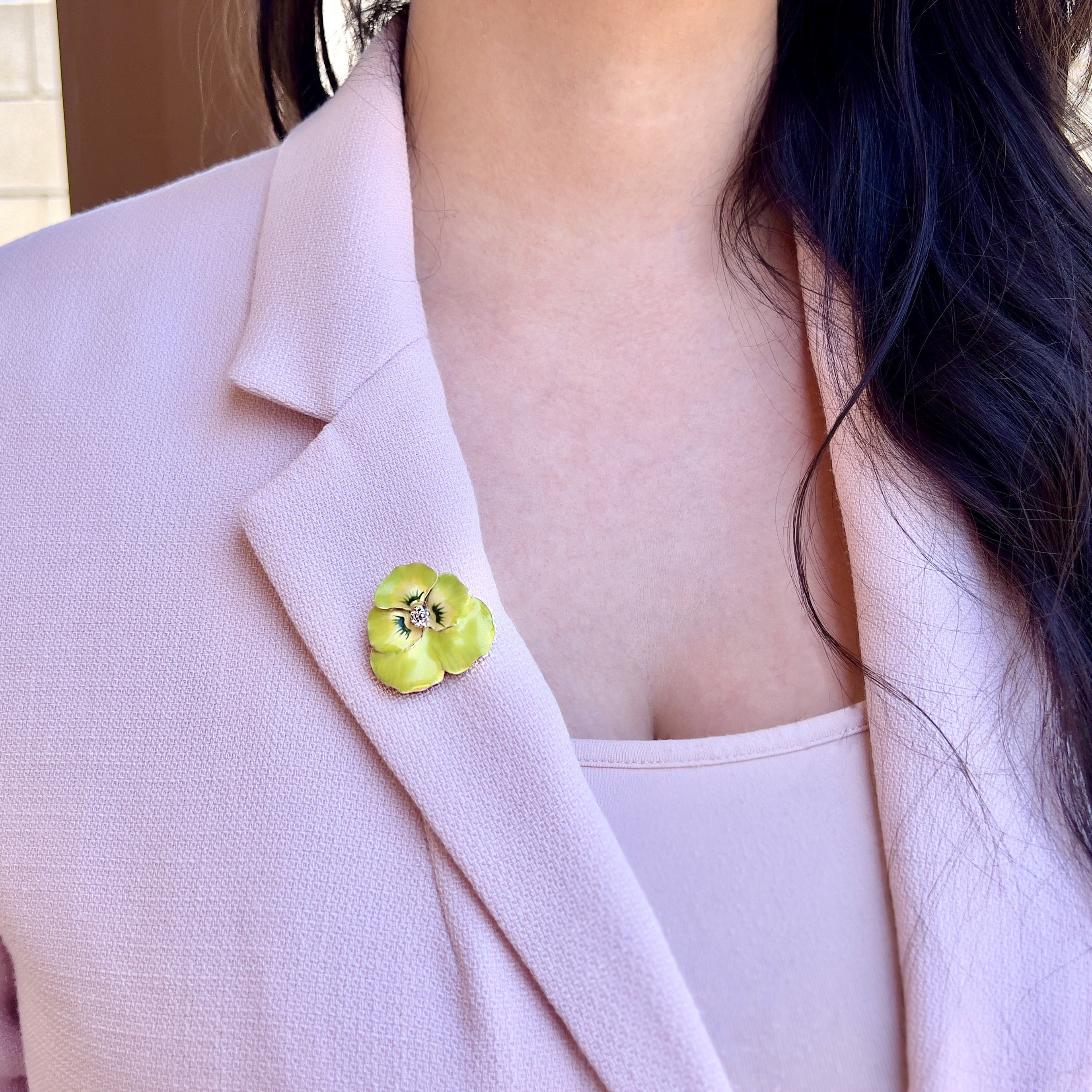 A person wearing a lime green pansy brooch on their pink blazer. 